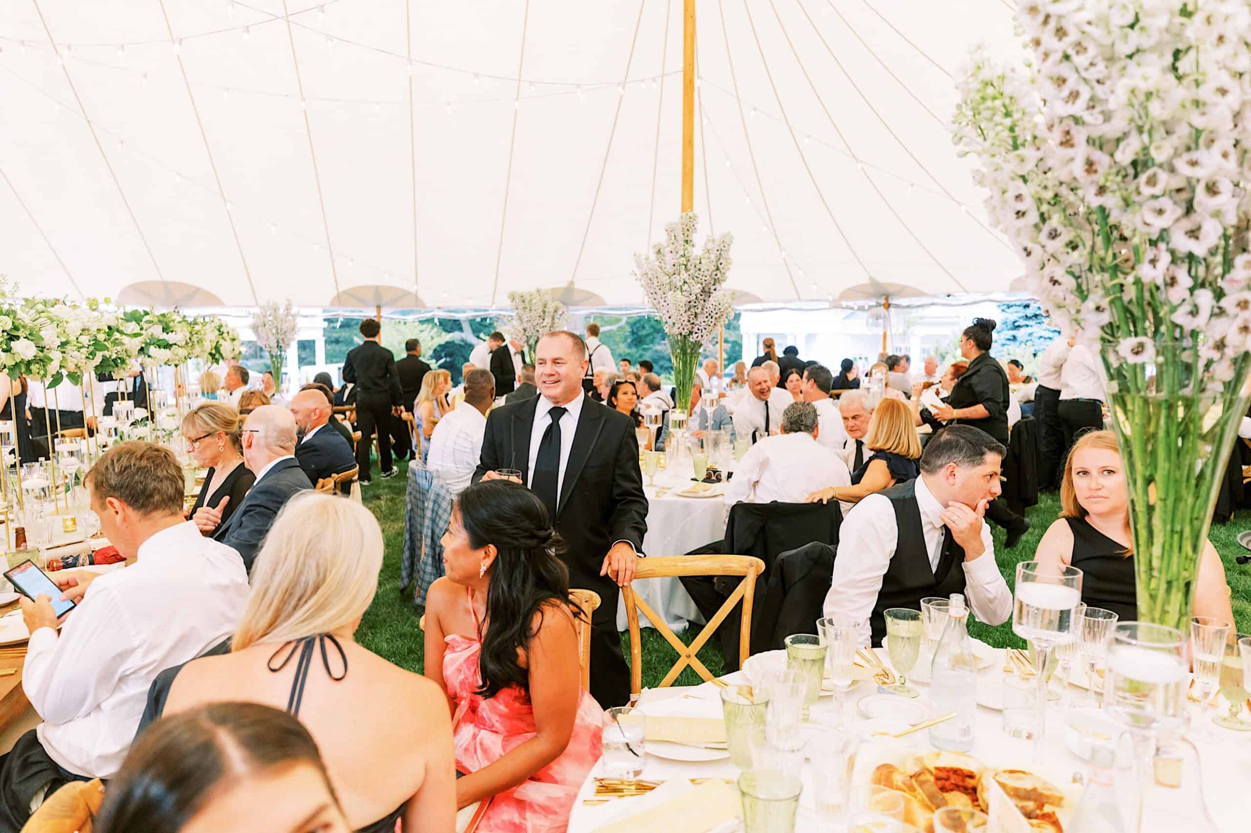 Guests seated at decorated tables under a large white tent at a romantic backyard wedding in NJ; people are eating, talking, and mingling.