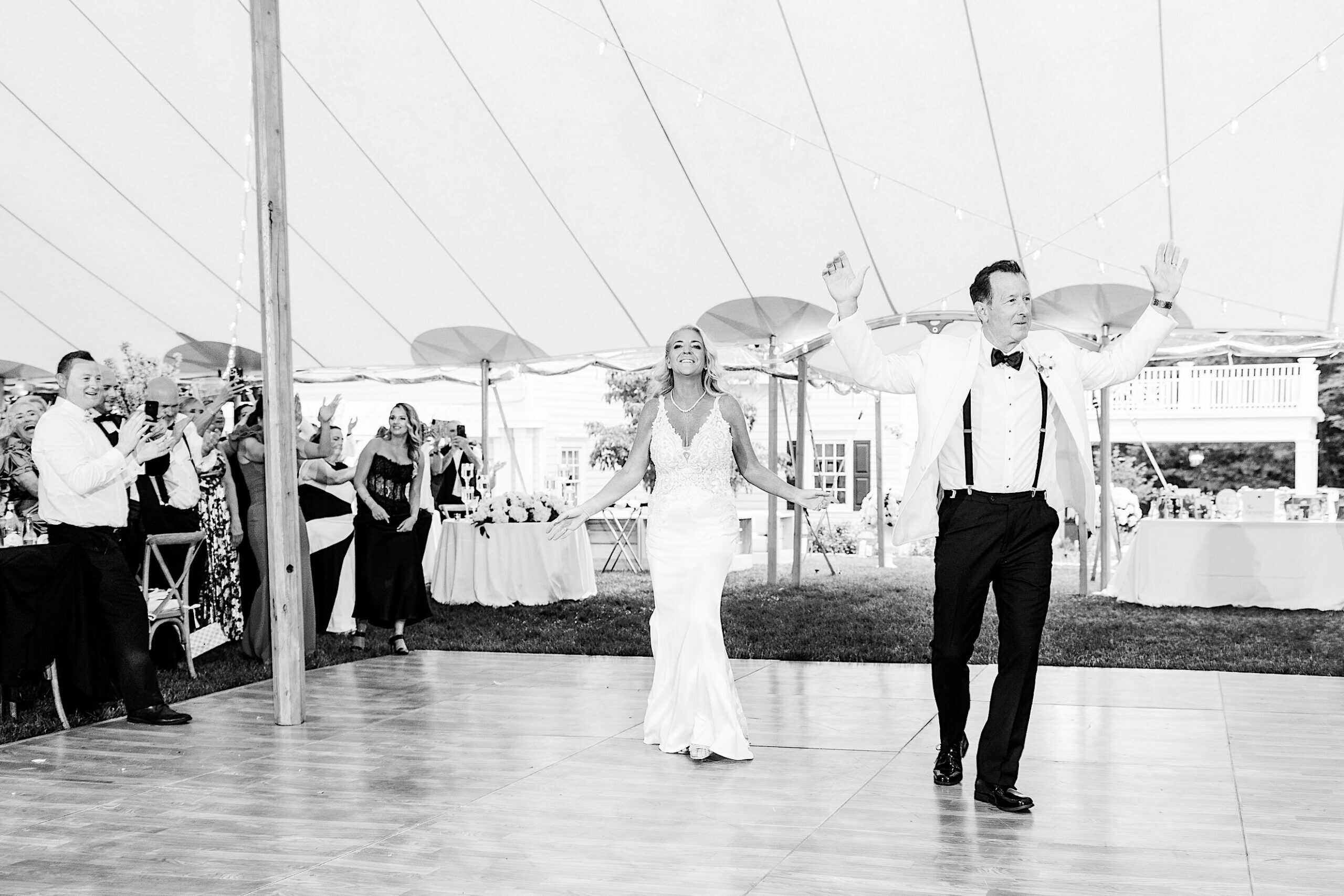 A bride and groom enter their romantic backyard wedding in NJ, smiling and raising their hands as guests applaud under the reception tent.