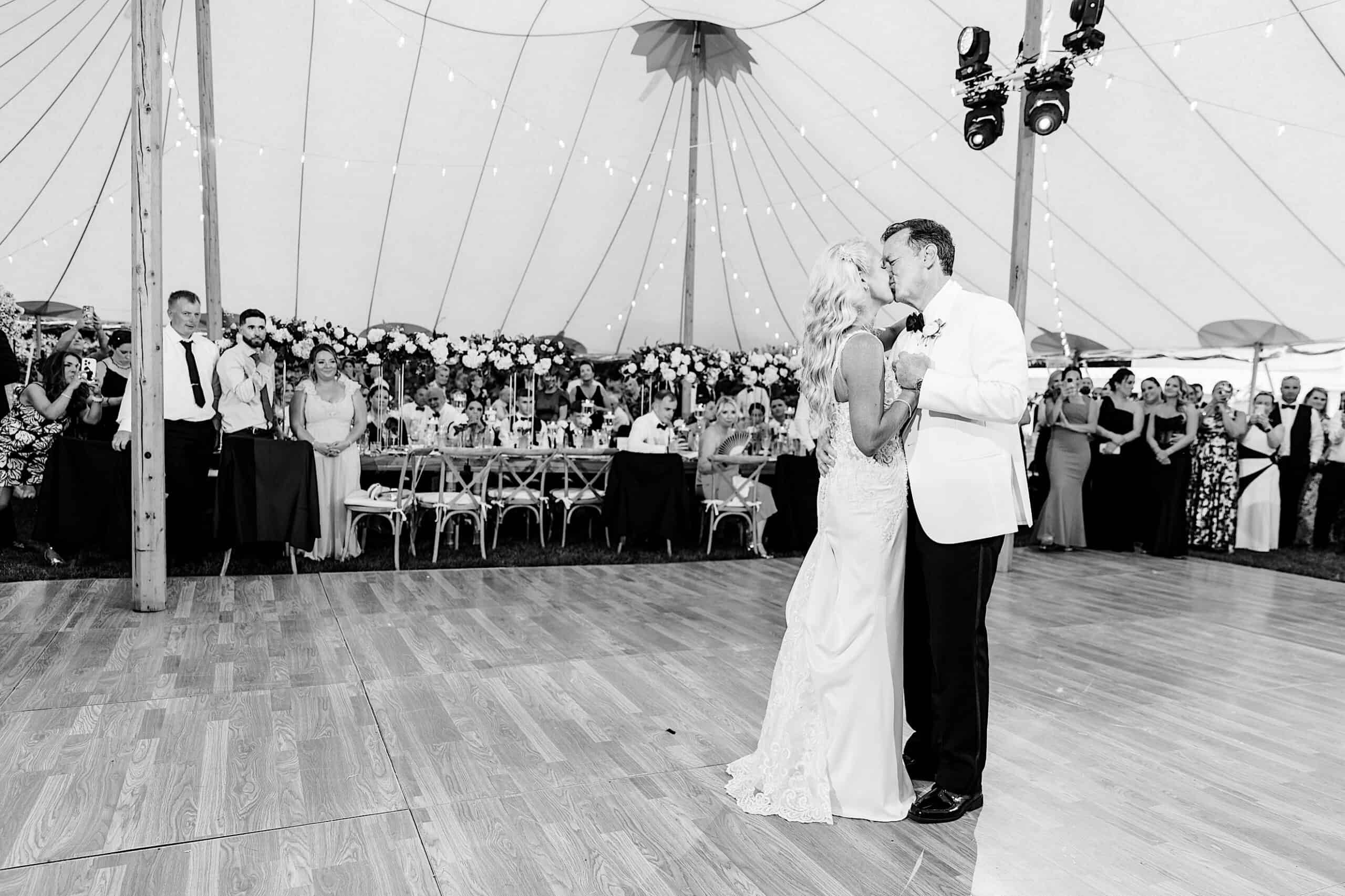 A bride and groom share their first dance under a tent at their romantic backyard wedding in NJ, surrounded by seated and standing guests watching them.