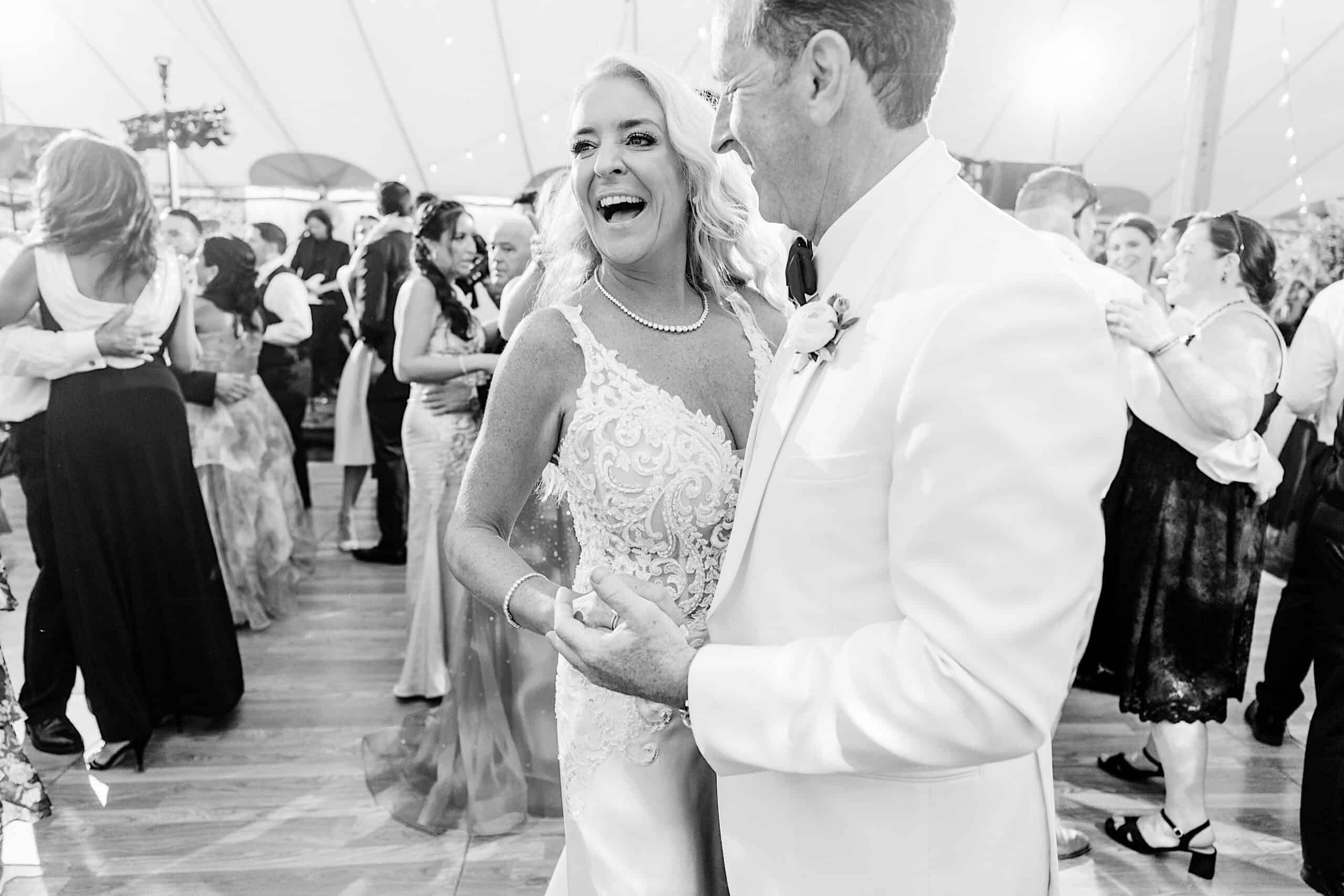 A bride and groom dance together at their romantic backyard wedding in NJ, surrounded by guests on a crowded dance floor under a tent.