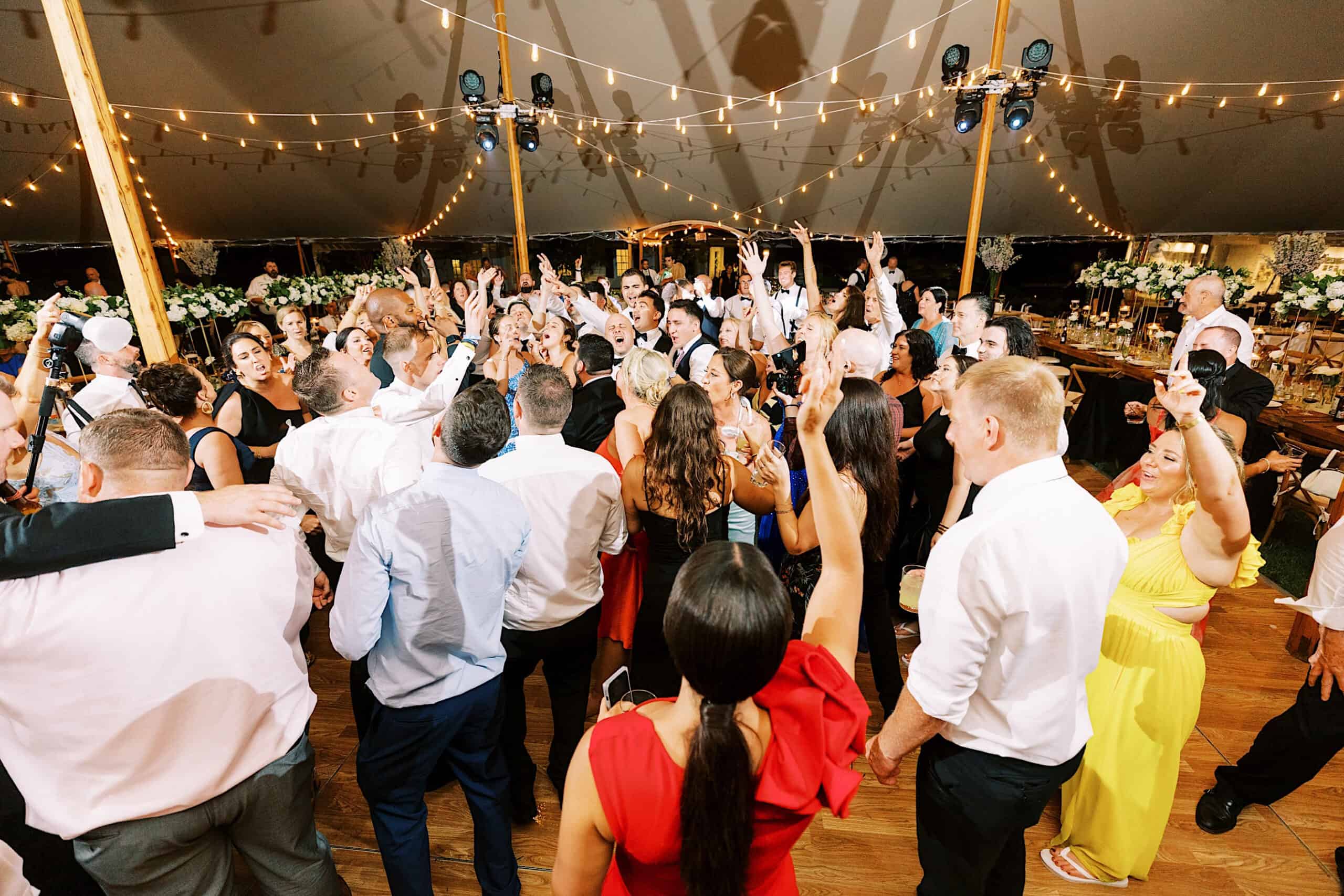 A large group of people dance and celebrate under a tent with string lights at a romantic backyard wedding in NJ.