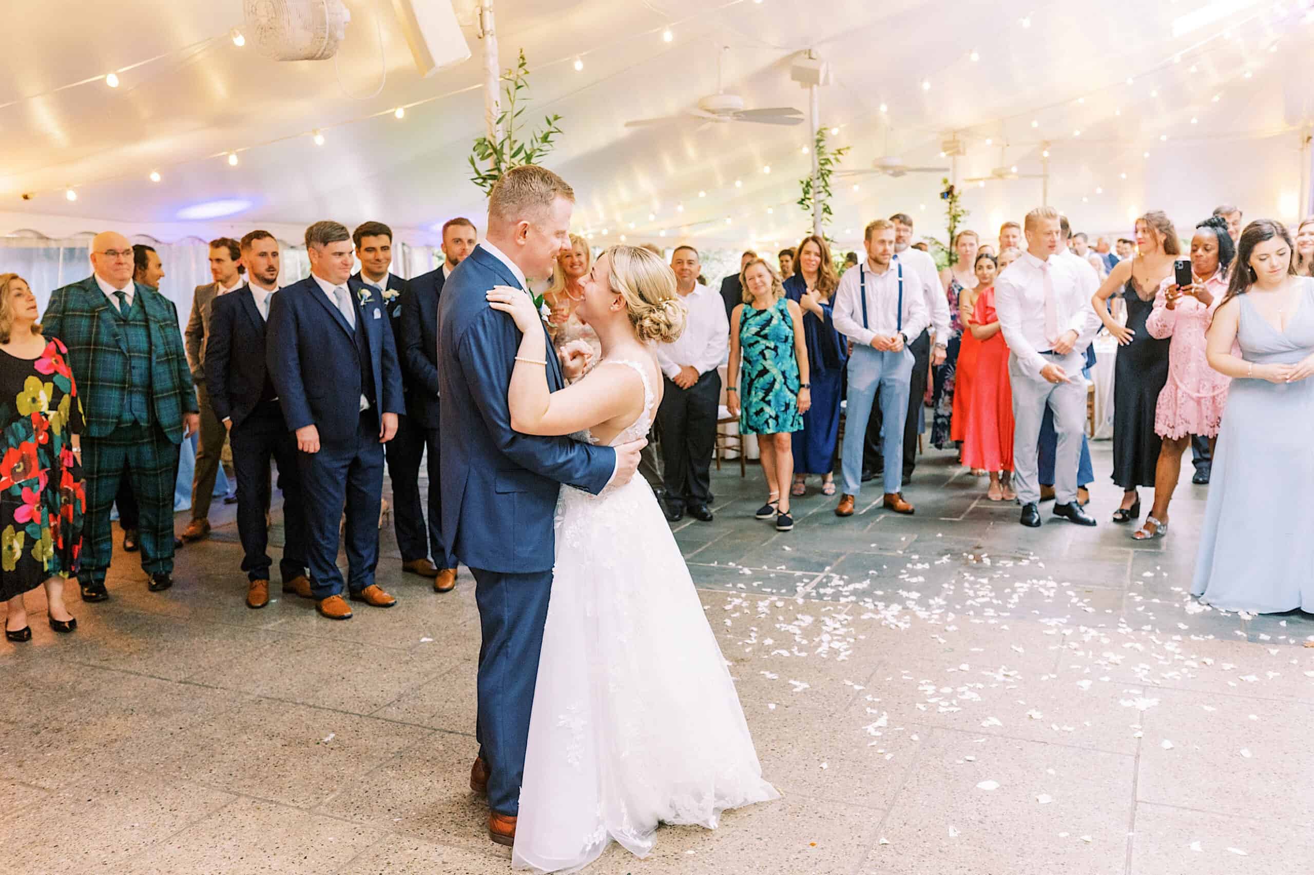 A bride and groom share their first dance at a summer wedding at Appleford Estate, surrounded by standing guests under a white tent with string lights.
