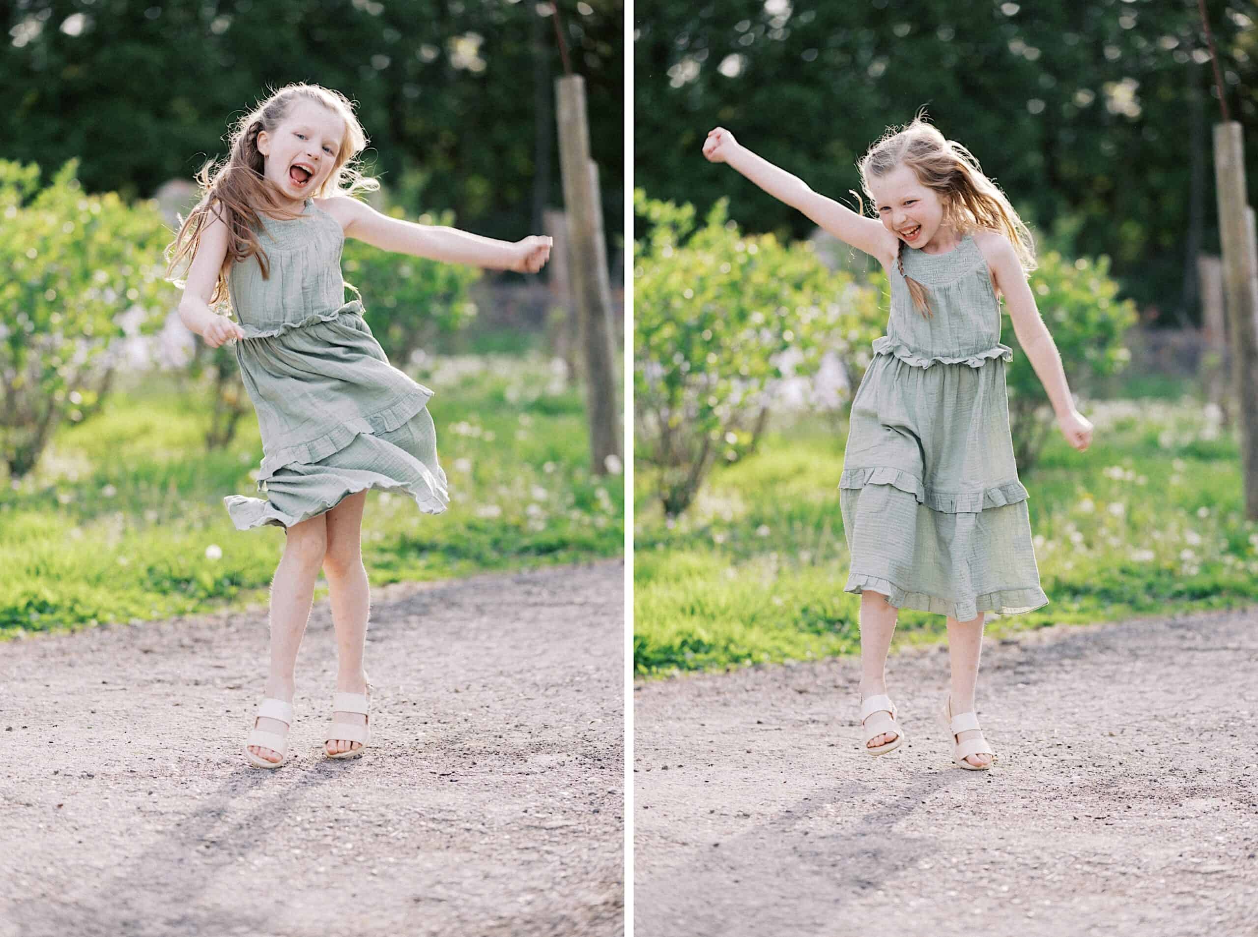 A young girl in a light green dress and sandals is seen jumping and dancing outdoors on a dirt path with greenery in the background.
