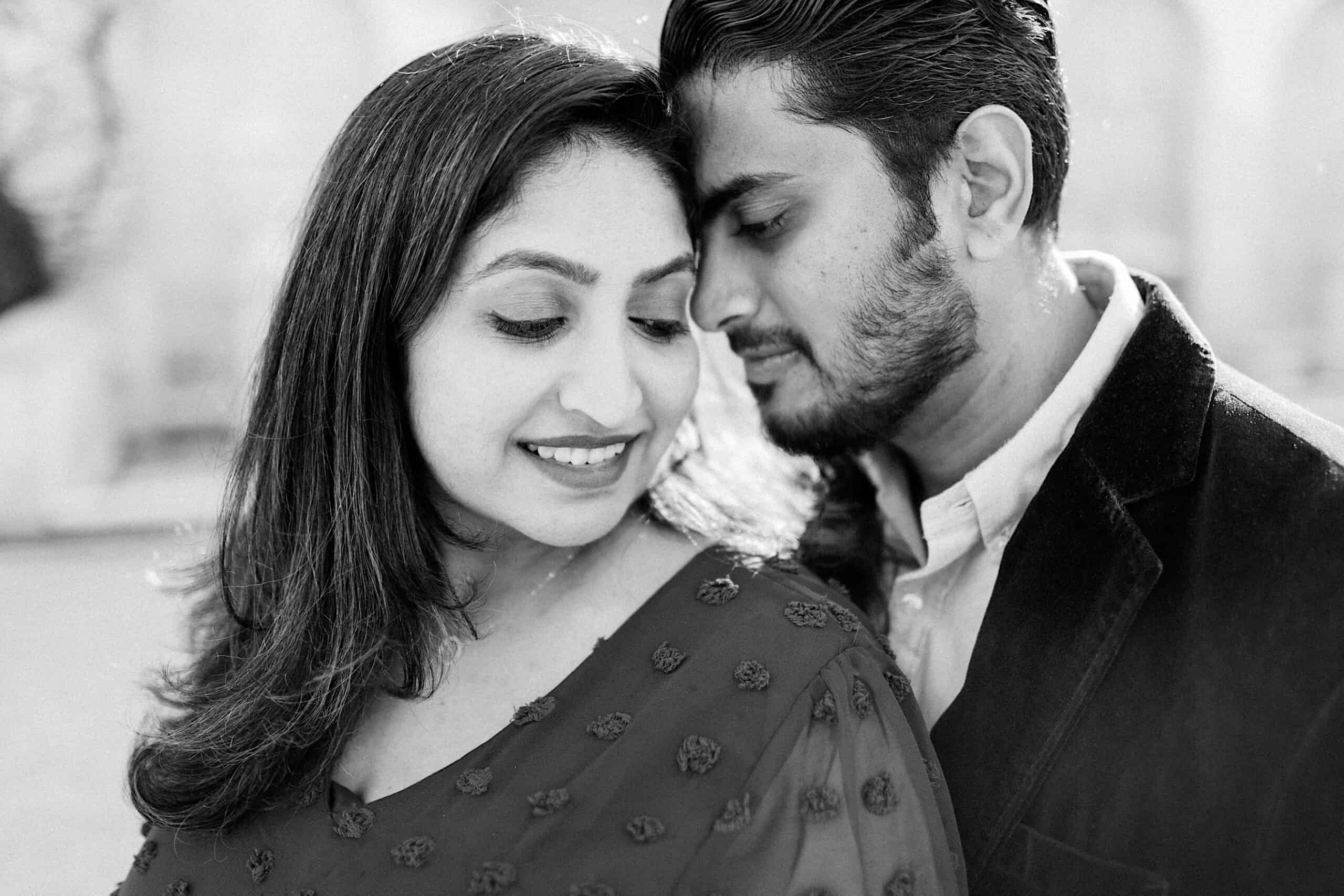 A woman smiles while a man leans his forehead close to her temple; both have their eyes closed in a calm, intimate moment.