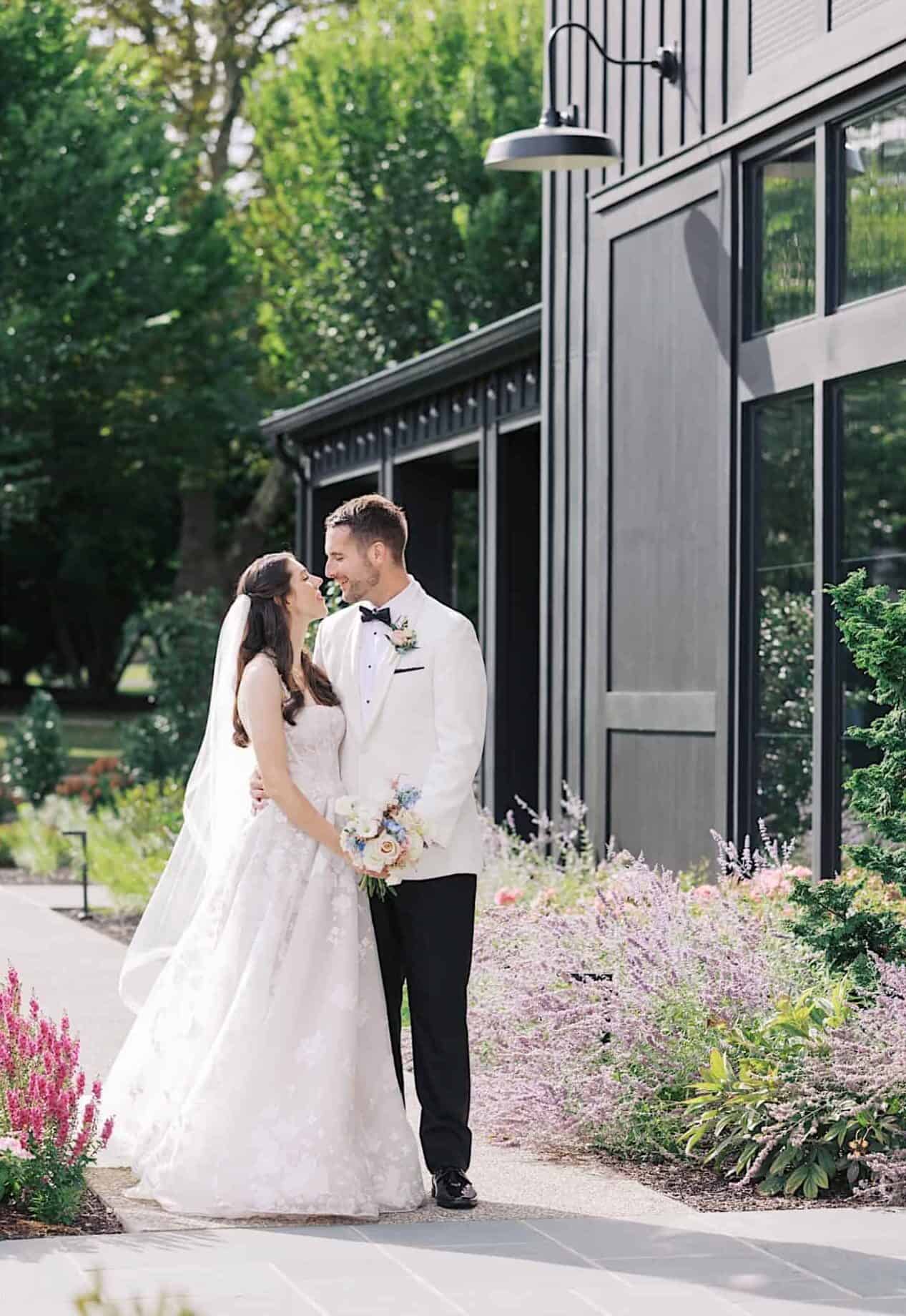 A bride in a white floral dress holds a pastel bouquet; next to it, a bride and groom smile outside a modern building surrounded by greenery during their luxurious wedding at The Ivy at Ellis Preserve.