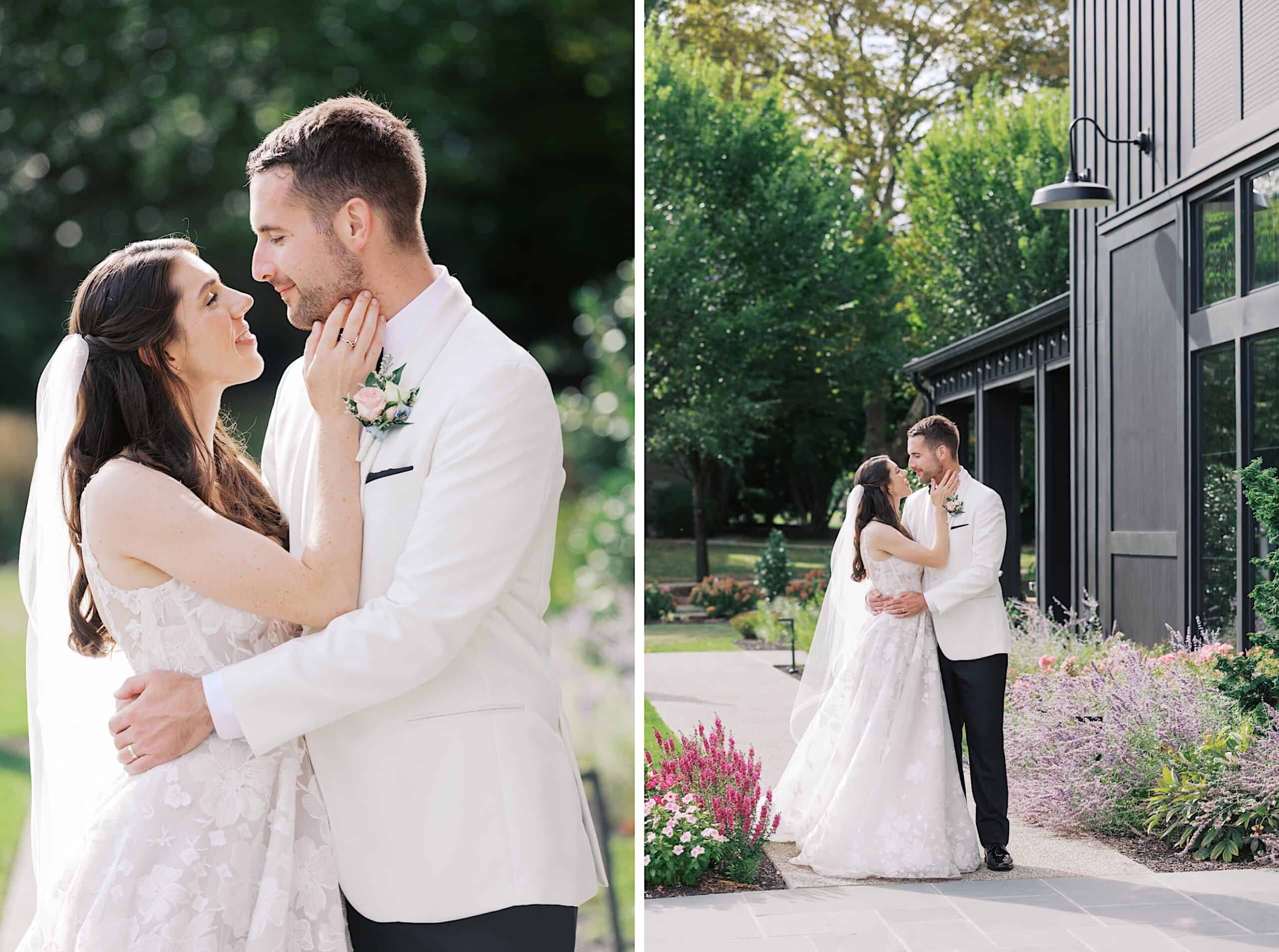 A bride and groom in formal attire embrace and gaze at each other outdoors near a black building, surrounded by greenery and flowers, capturing a romantic moment from their luxurious wedding at The Ivy at Ellis Preserve.