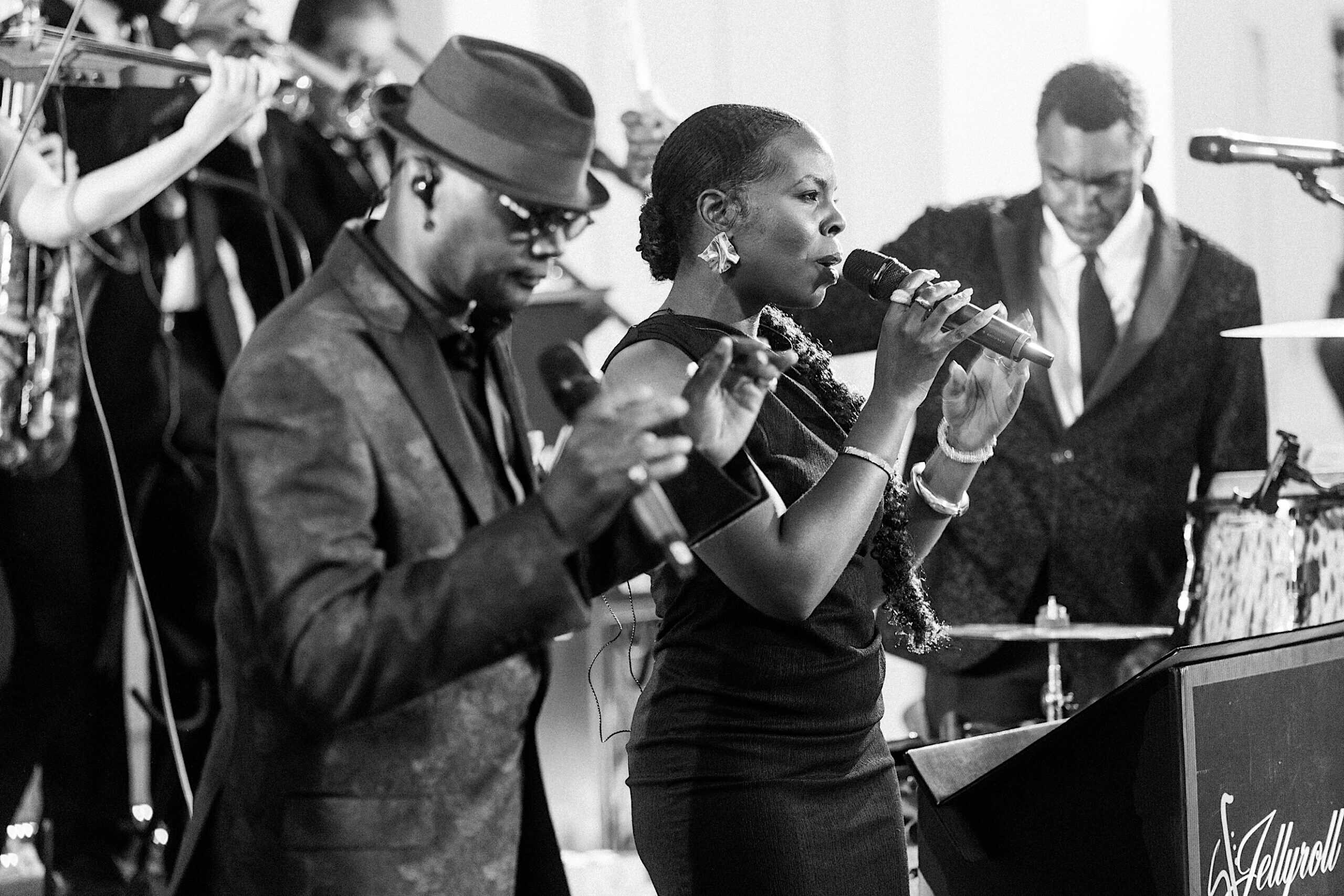 Black and white photo of a band performing at a luxurious wedding at The Ivy at Ellis Preserve; a man and woman sing with microphones as another plays keyboard in the background.
