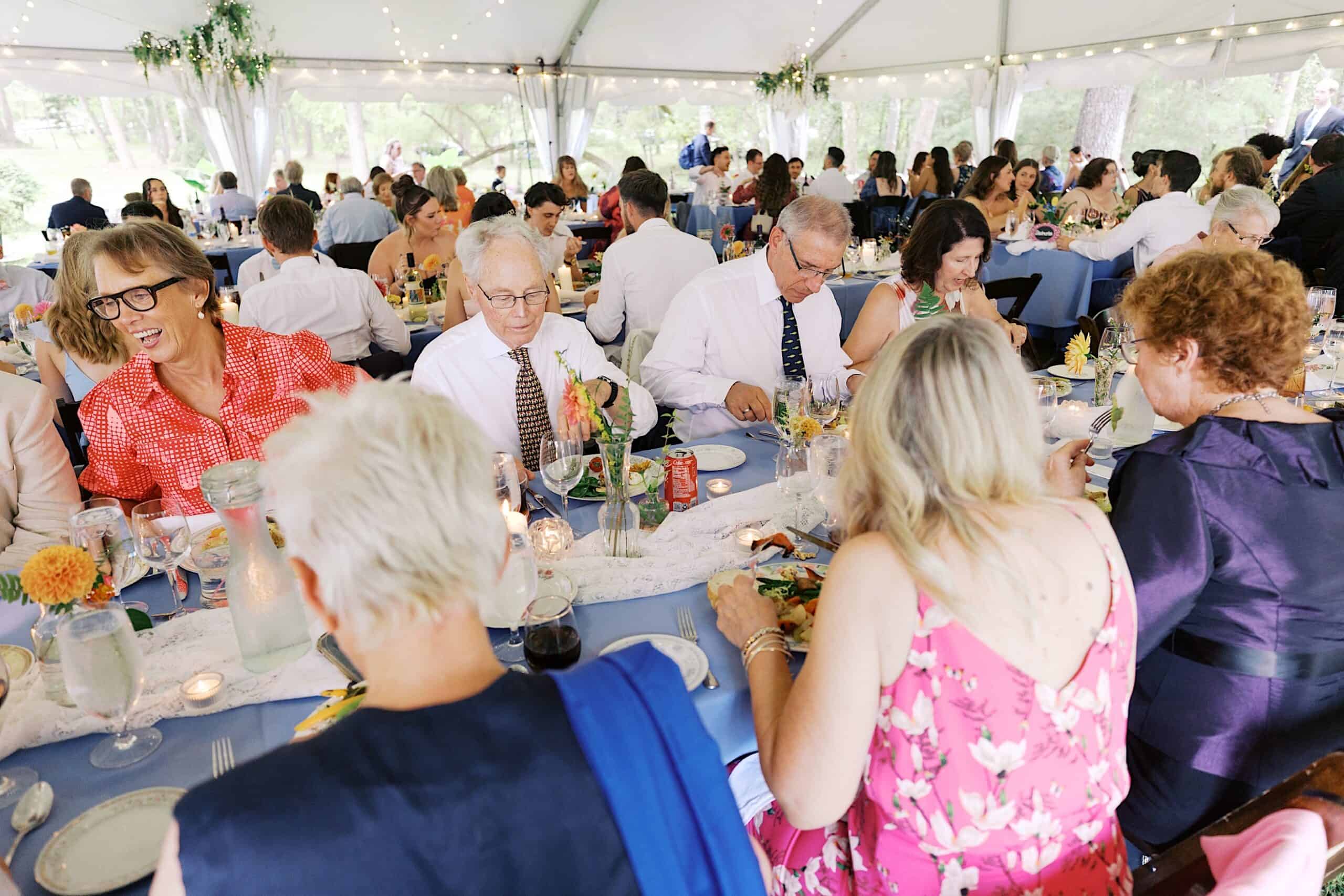 Guests seated at decorated tables eat and converse under a white tent during a beautiful wedding at Vincent Forge Mansion.