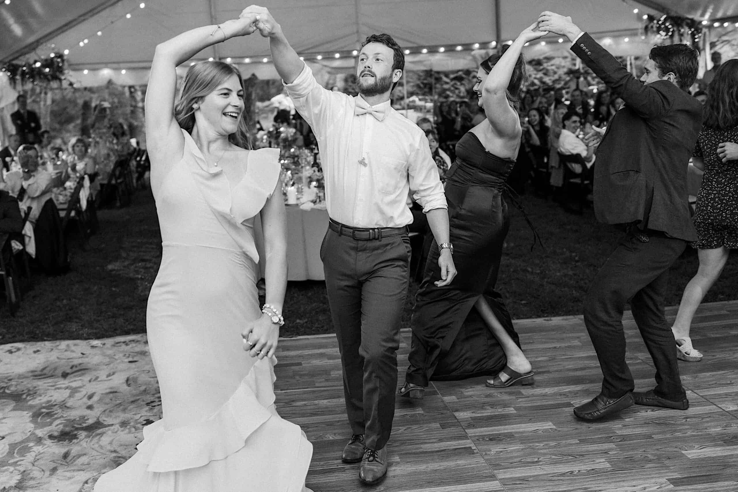 Four people are dancing in pairs under a tent at a beautiful wedding at Vincent Forge Mansion, with tables and guests visible in the background.