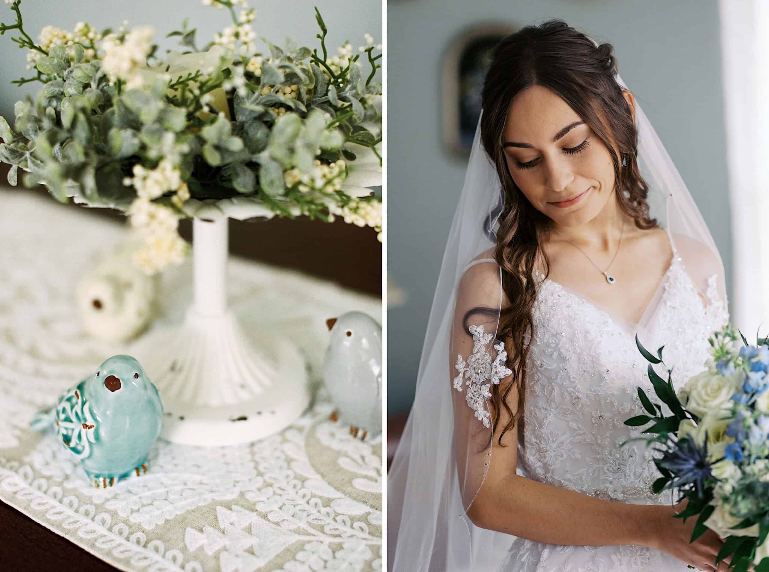 A bride in a white dress holding a bouquet stands beside a decorative table with ceramic blue birds and greenery on a white lace tablecloth at a beautiful Lochwood Manor wedding.