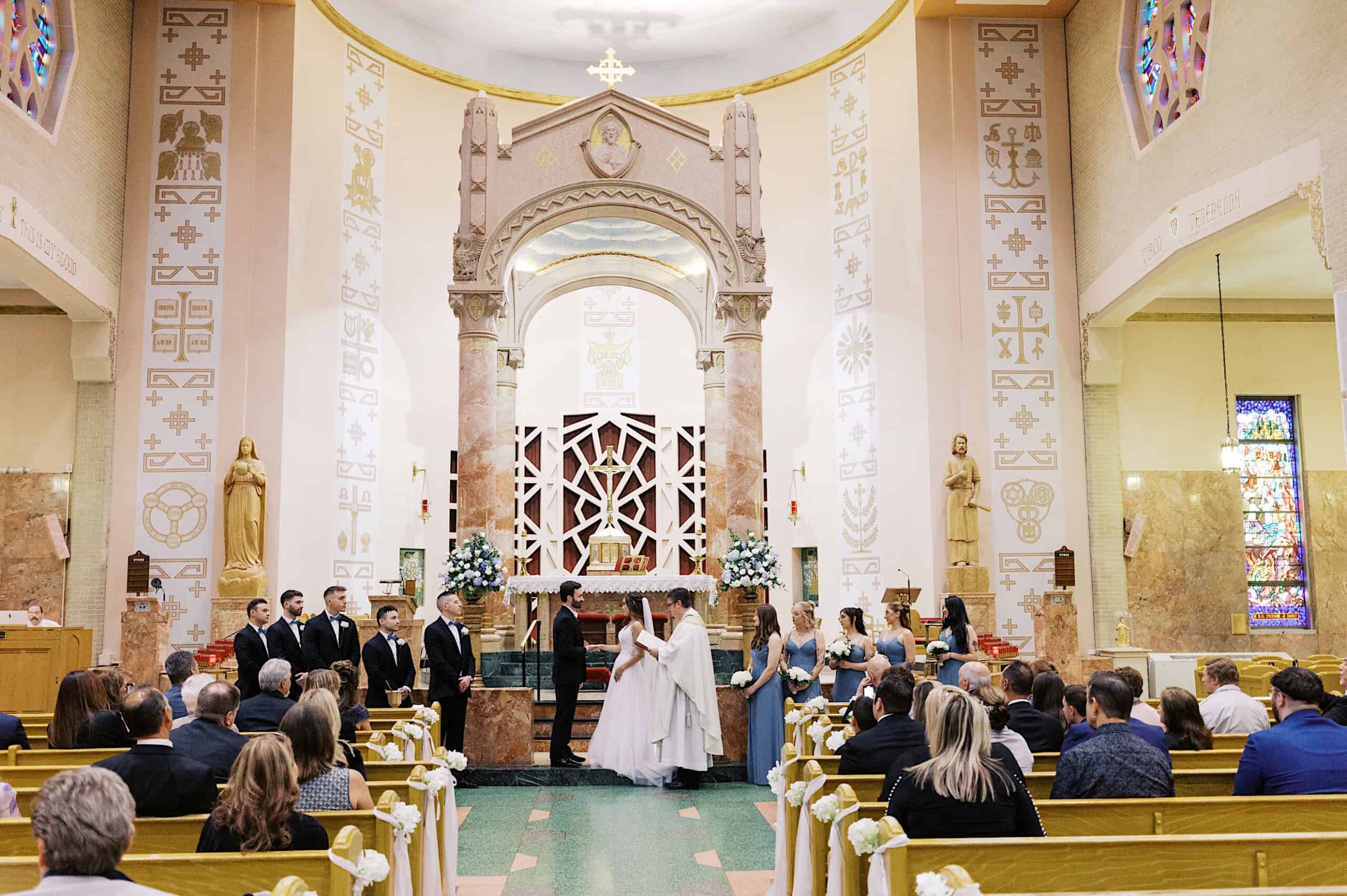 A beautiful Lochwood Manor wedding ceremony inside a church, with guests seated in pews, the couple standing at the altar, and their wedding party members on either side.