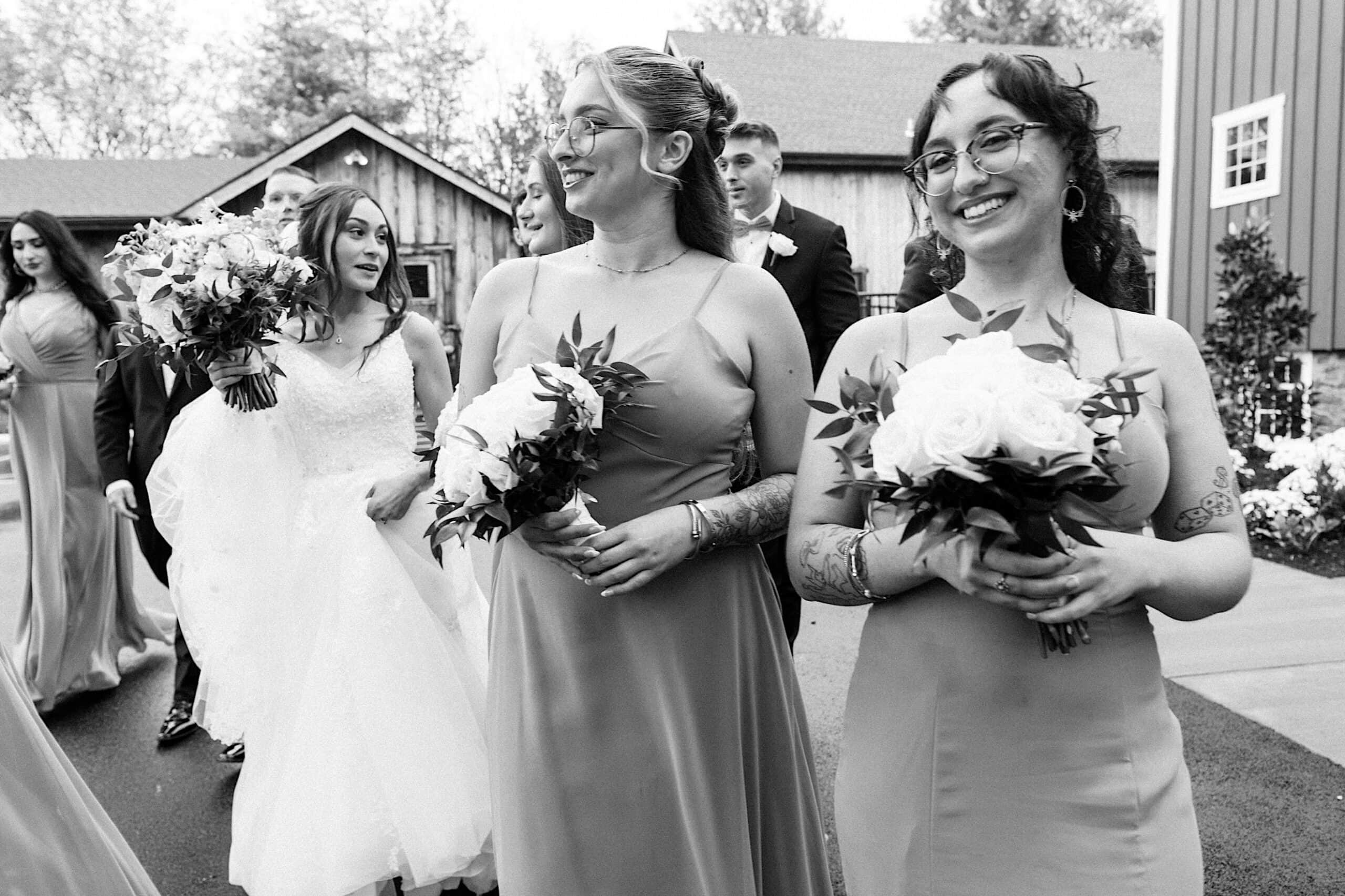 A group of people in formal attire, including bridesmaids holding bouquets, walk together outdoors at a beautiful Lochwood Manor wedding.
