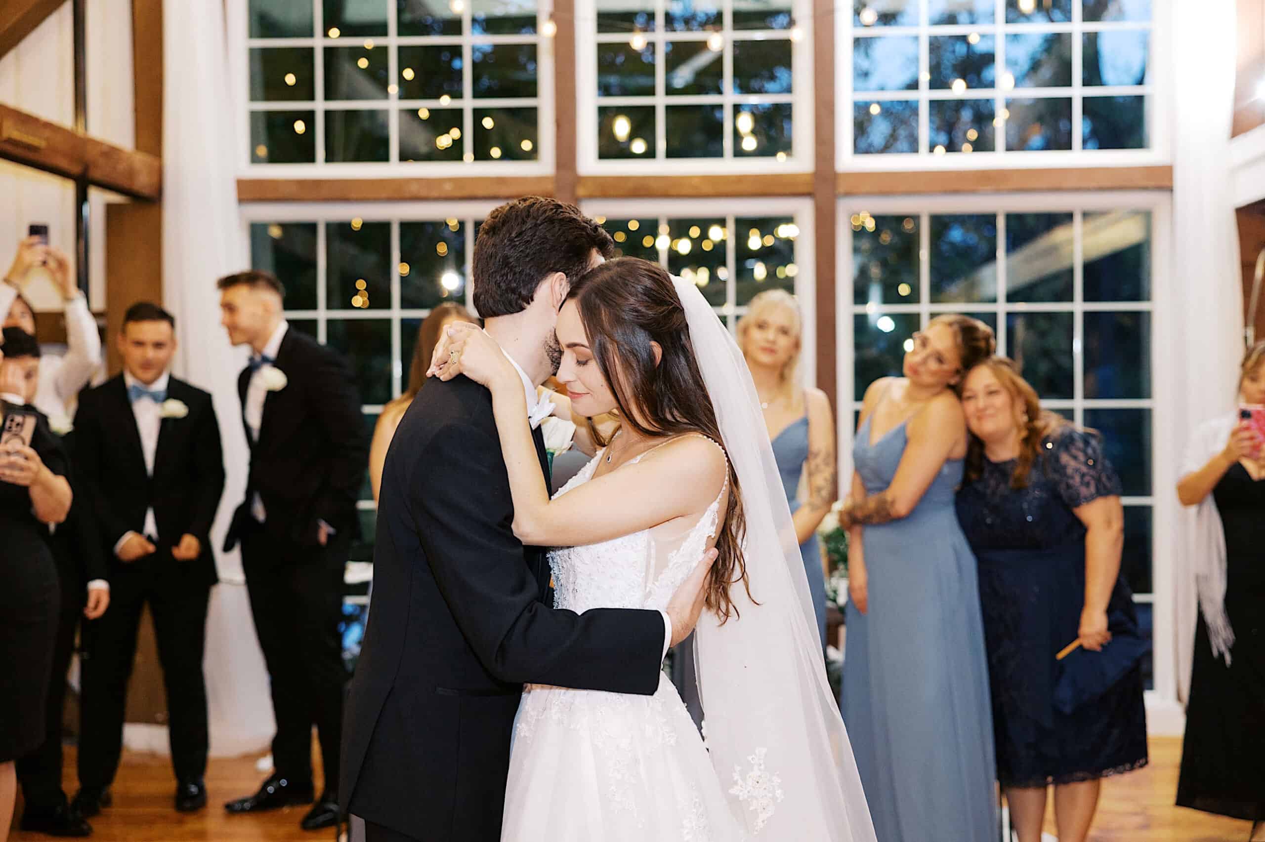 A bride and groom share their first dance at a beautiful Lochwood Manor wedding, surrounded by guests who watch and take photos.