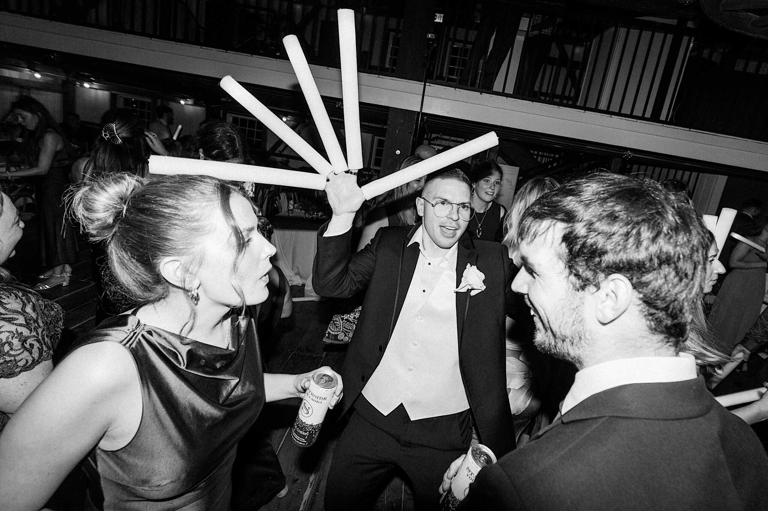 A man in a suit holds up several light sticks while dancing with two other people at a beautiful Lochwood Manor wedding party.