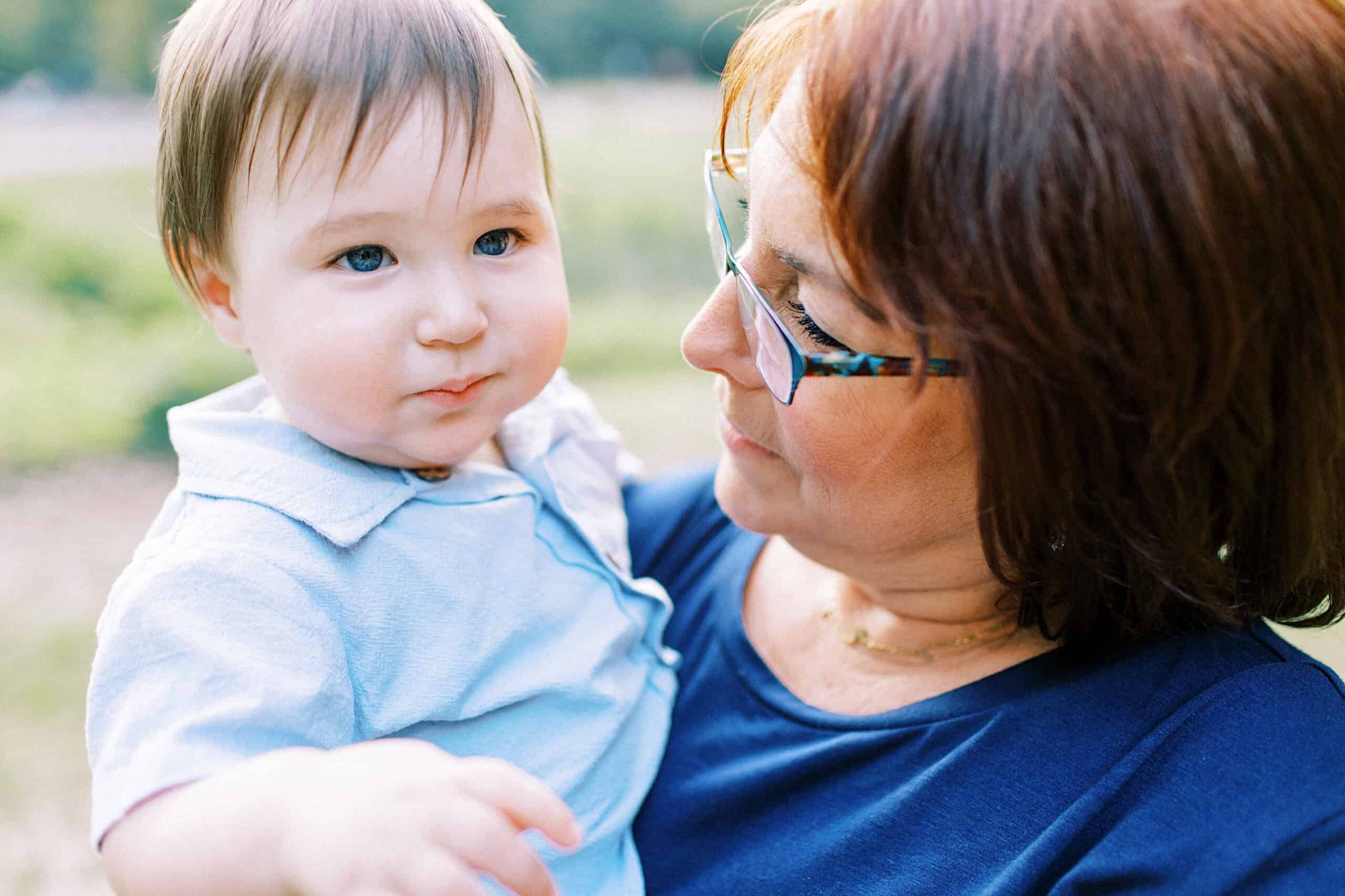 A woman wearing glasses holds a young child with light brown hair outdoors during Spring Family Photos in Bucks County. Both are looking in different directions.