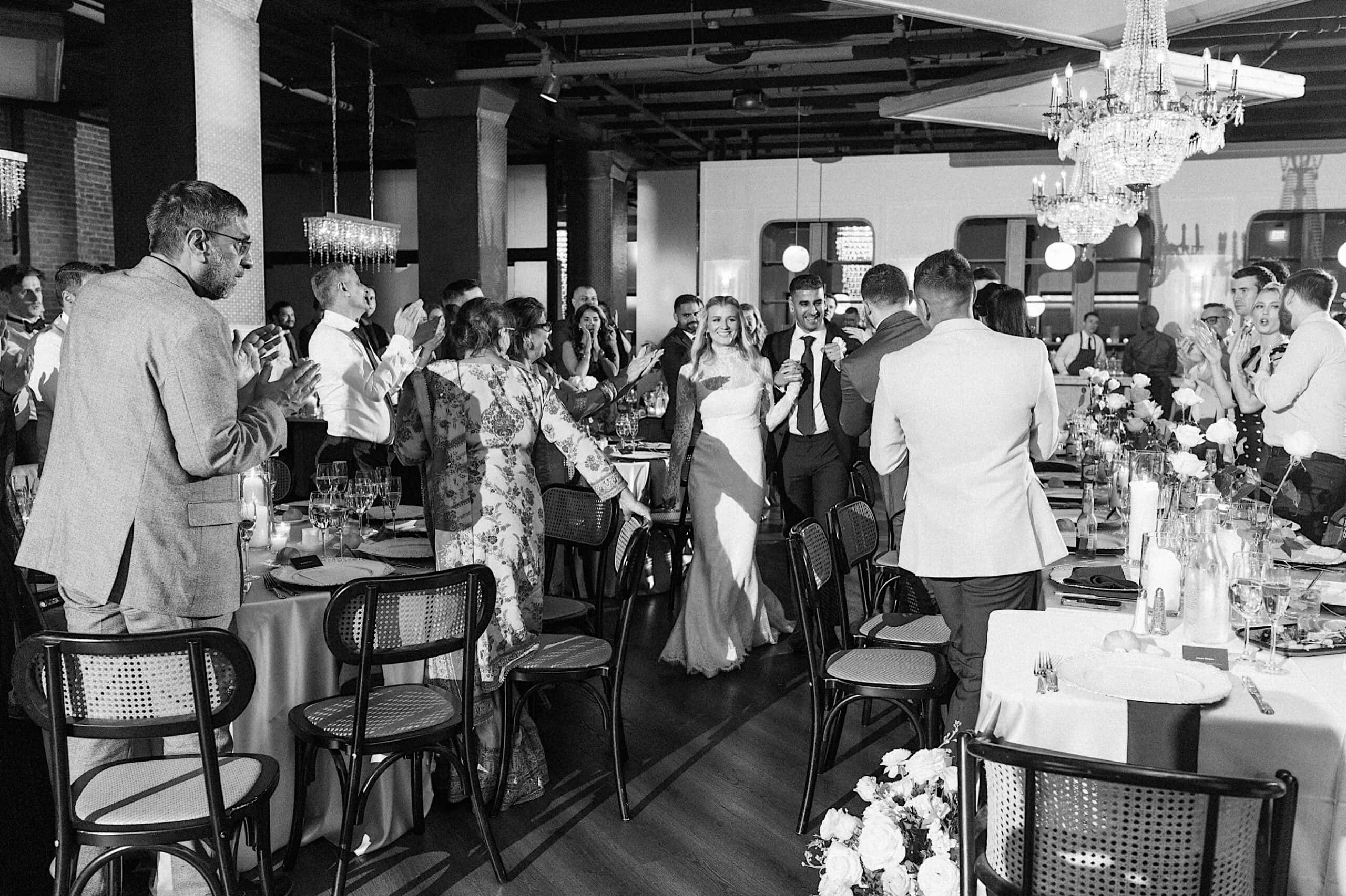 An elegant Philadelphia Cescaphe Wedding at Tendenza unfolds as the bride and groom enter a beautifully decorated reception hall, with guests standing and applauding, and tables set for a formal celebration.