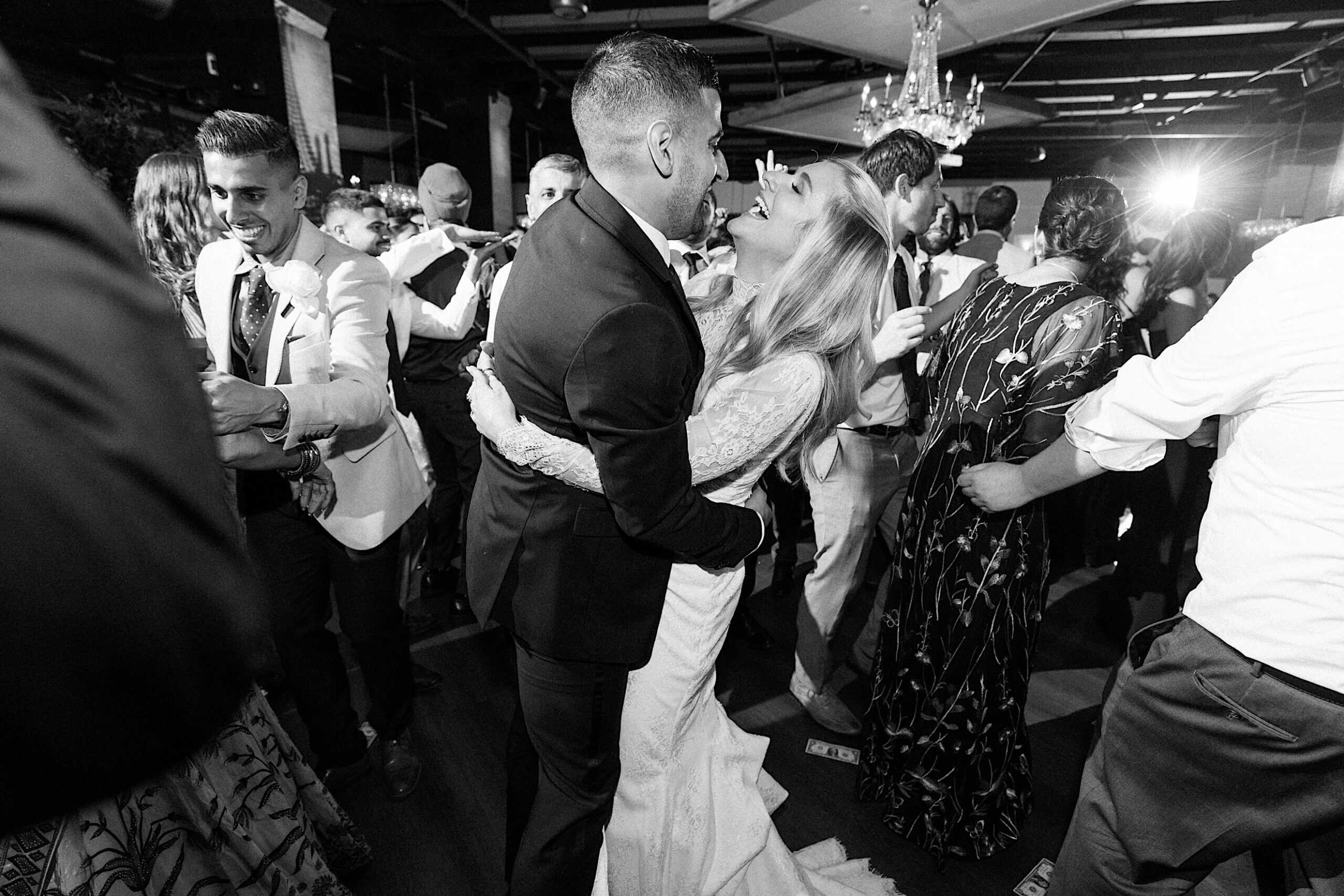 A bride and groom embrace and smile at each other while dancing, surrounded by guests on a crowded, lively dance floor during an elegant Philadelphia Cescaphe Wedding at Tendenza.