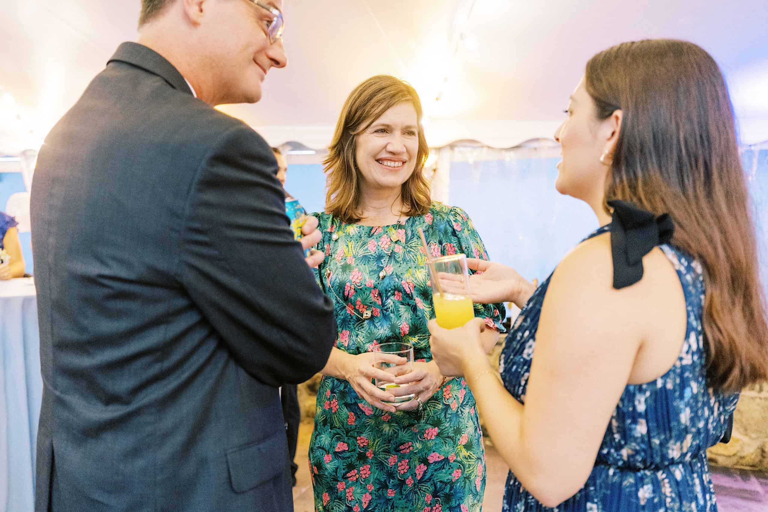 Three people stand together at a Summer Wedding at Appleford Estate, having a conversation and holding drinks under string lights.