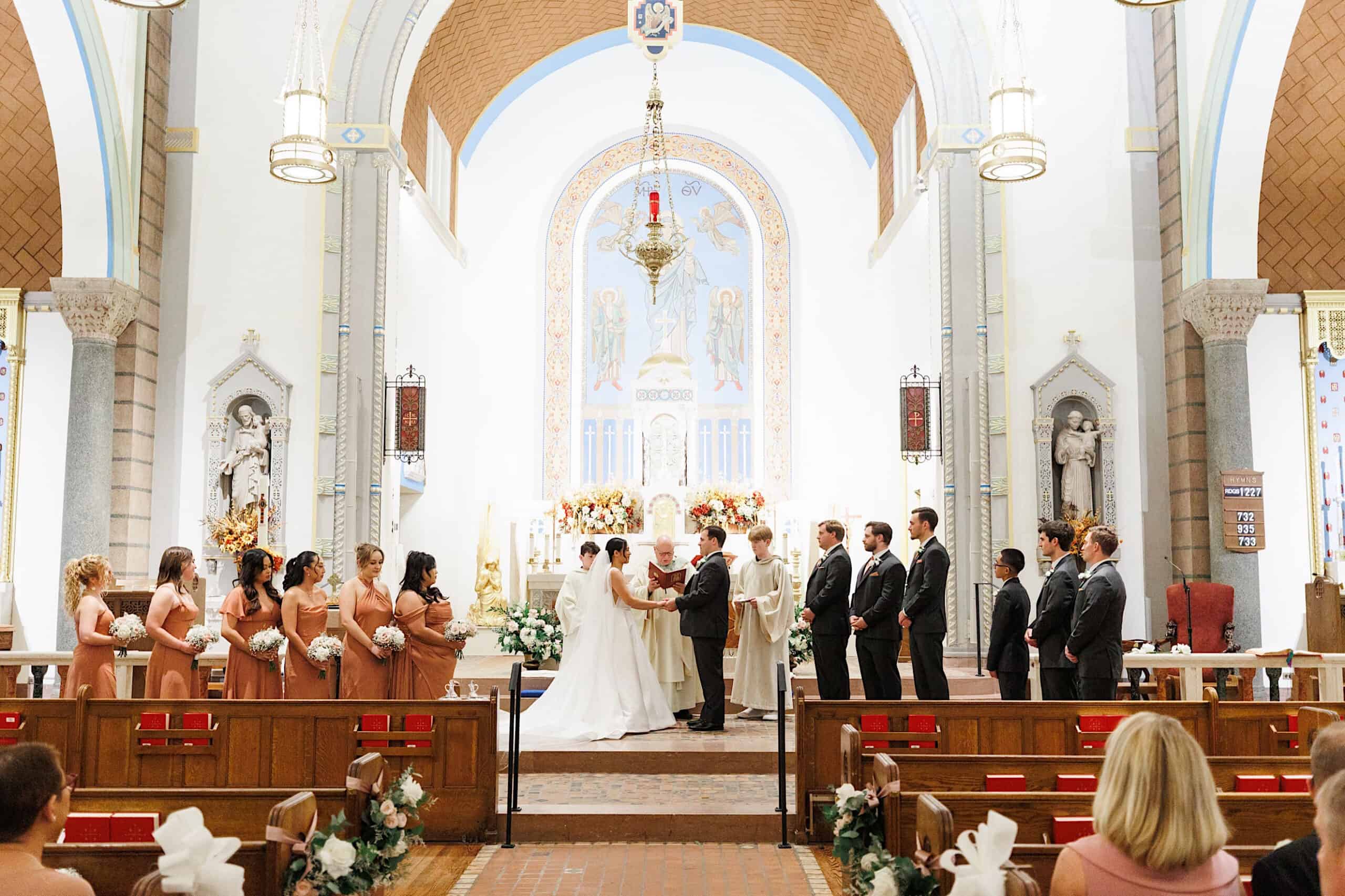A bride and groom stand at the altar with their wedding party inside a church during an elegant Cairnwood Estate Wedding ceremony.