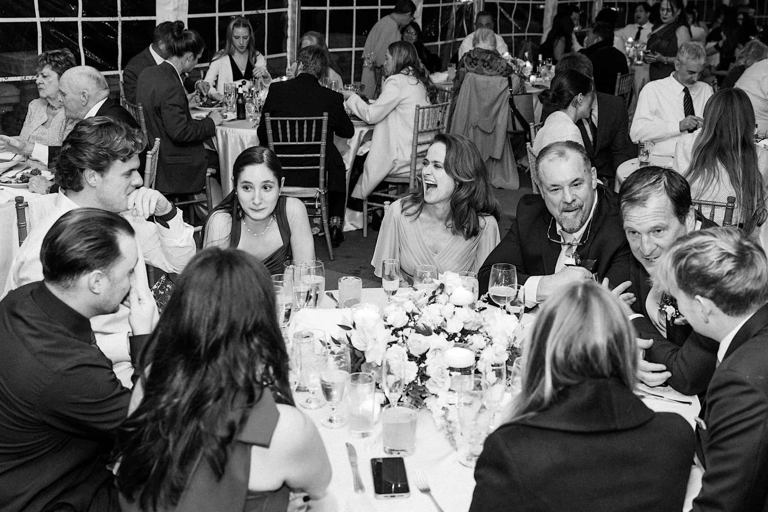A group of people seated around a table at an elegant Cairnwood Estate Wedding, engaged in conversation; other guests are visible in the background.