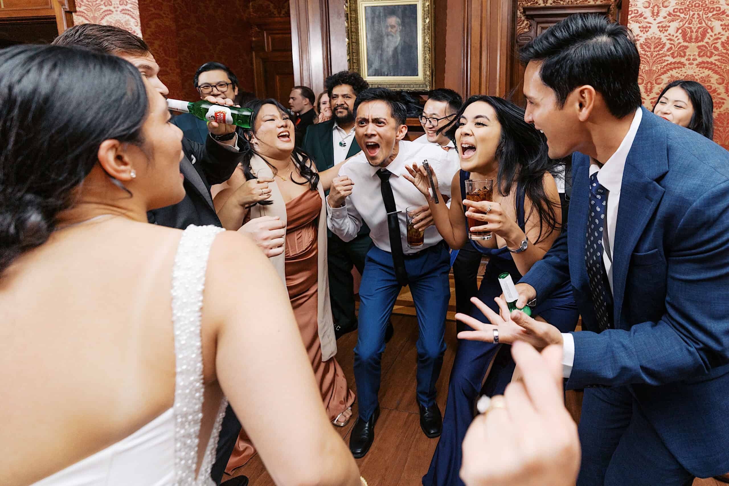 A group of people in formal attire cheer, laugh, and hold drinks while gathered in a lively circle at an elegant Cairnwood Estate Wedding.