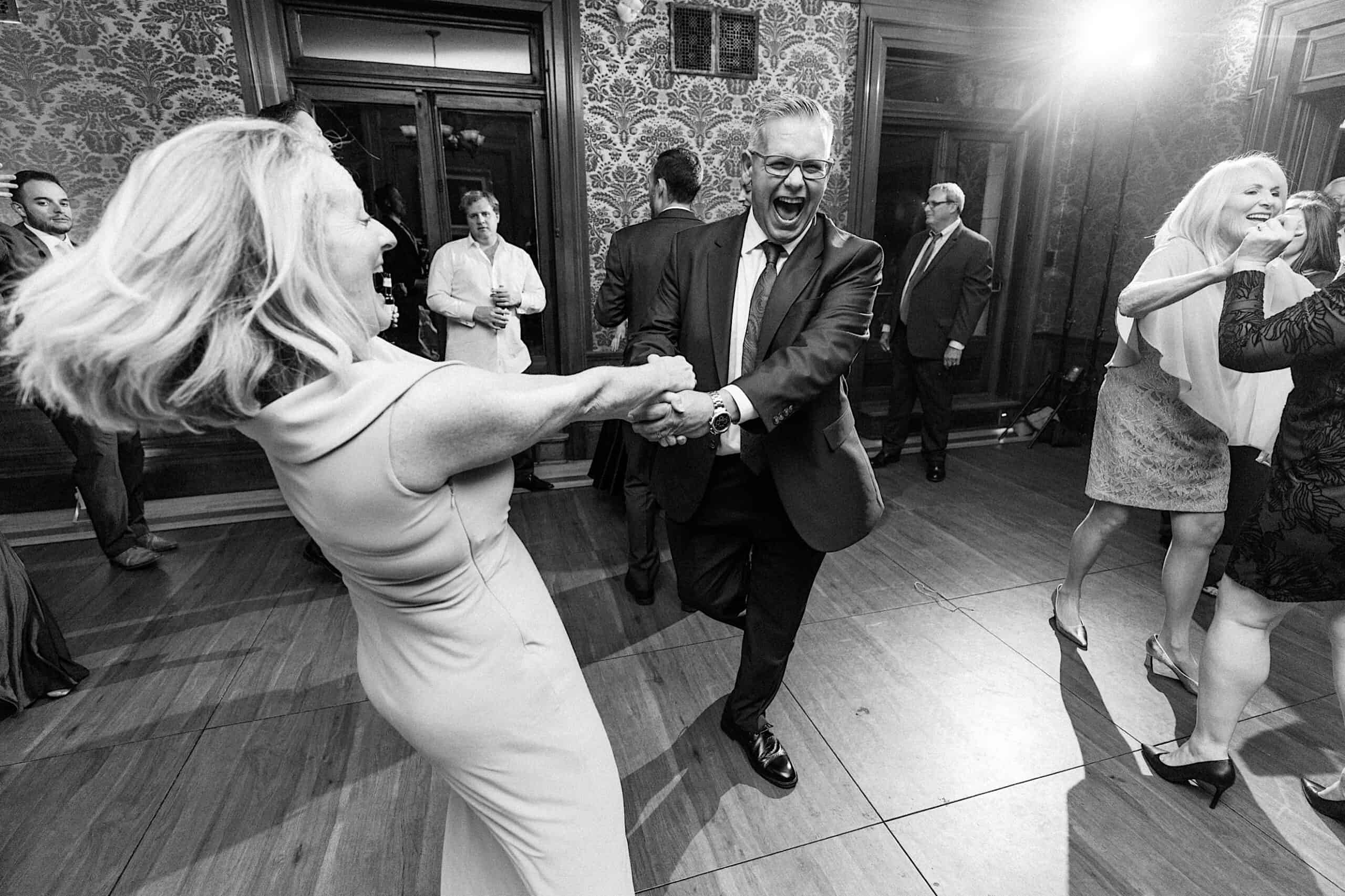 A man and woman dance energetically at an elegant Cairnwood Estate Wedding, while other guests stand and dance in the background.