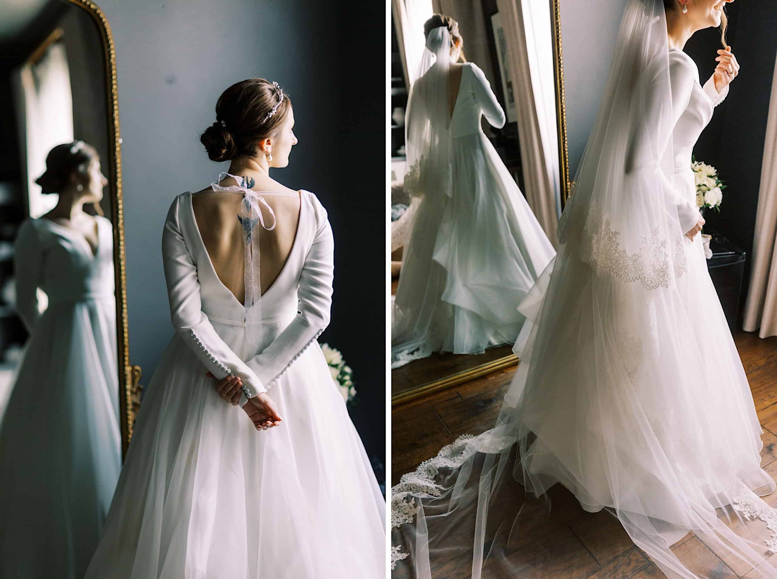 A bride in a long-sleeved white gown with an open back and bow stands by a large mirror at her Franklin Institute wedding, displaying her dress and veil from different angles.
