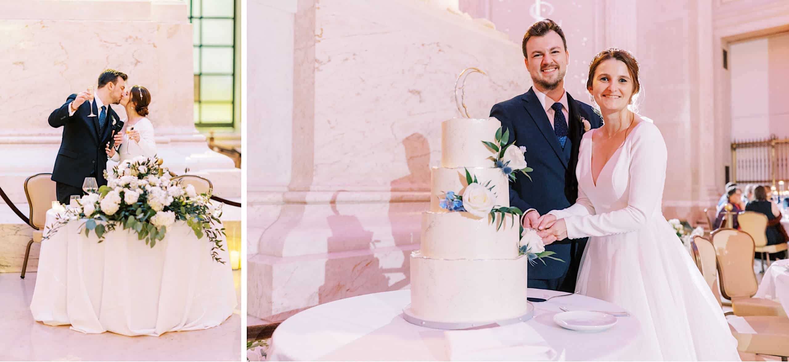 A bride and groom kiss behind a flower-adorned table and cut a three-tiered white wedding cake together at their elegant Franklin Institute wedding reception.