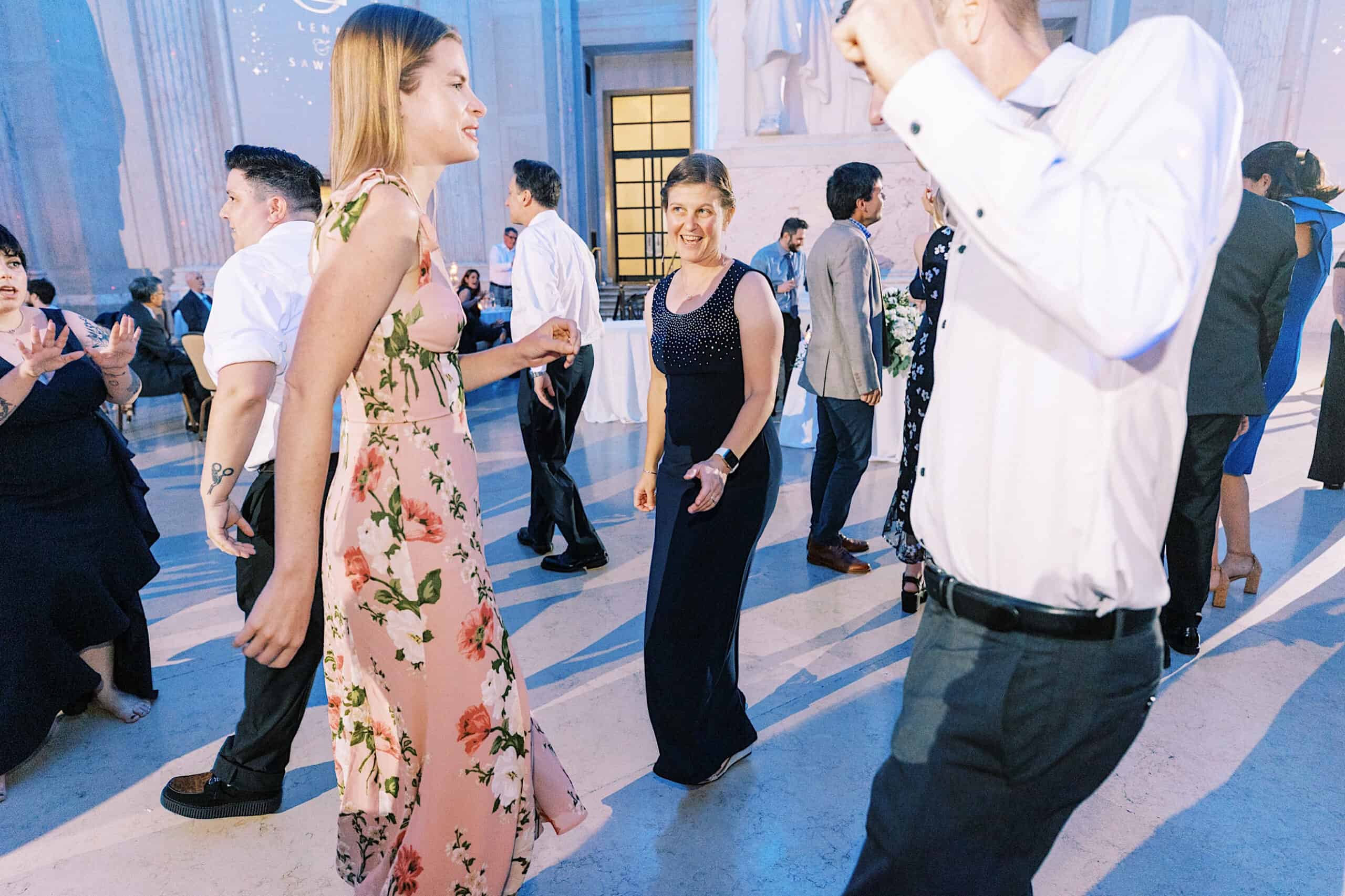 People dressed in formal attire dance together in a brightly lit indoor space with marble floors and high ceilings, capturing the elegance of a Franklin Institute wedding.