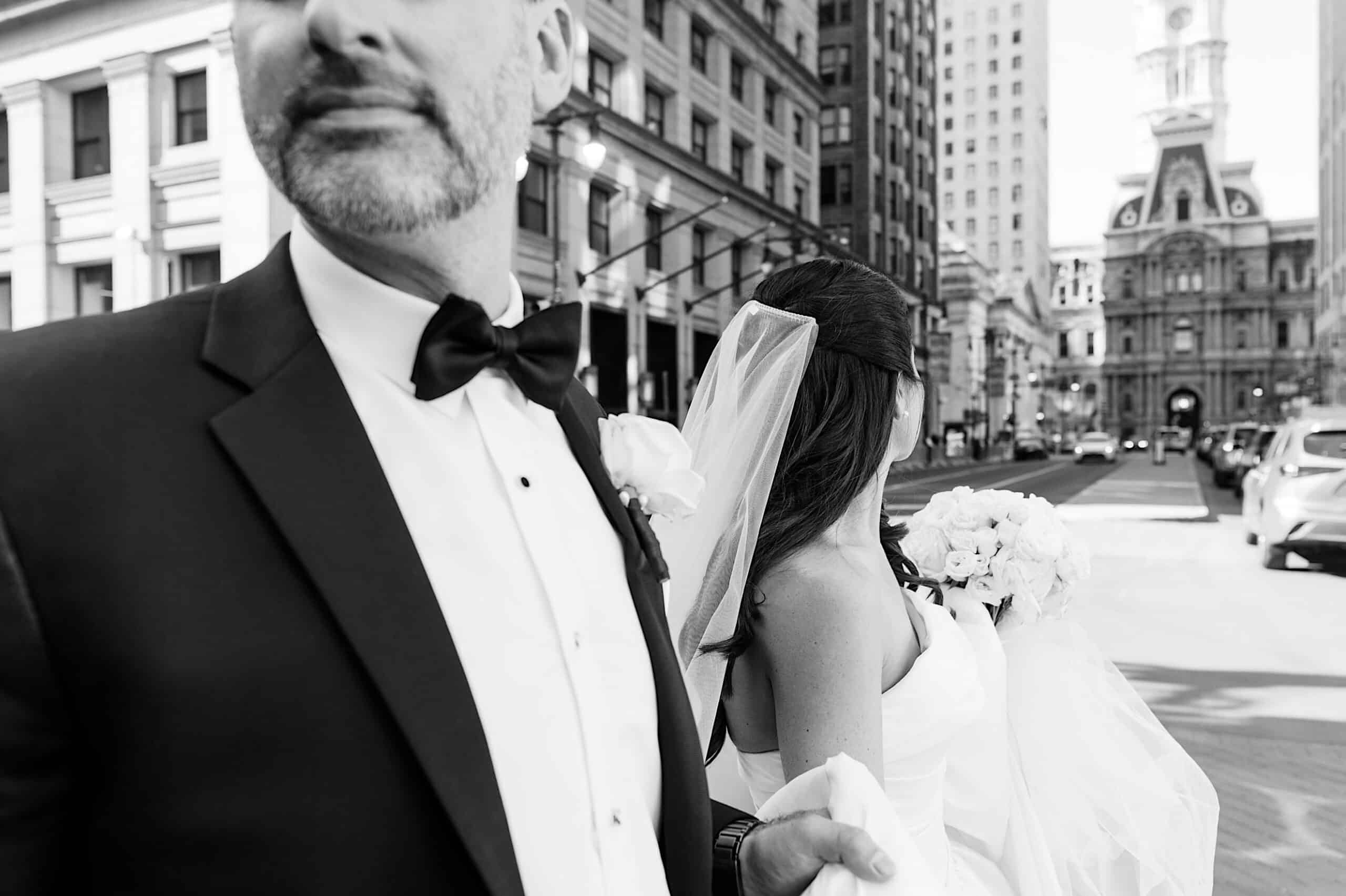A bride and groom in formal attire stand on a city street, with tall buildings and a historic structure behind them—capturing the romance of a Classic Wedding at Ballroom at the Ben.