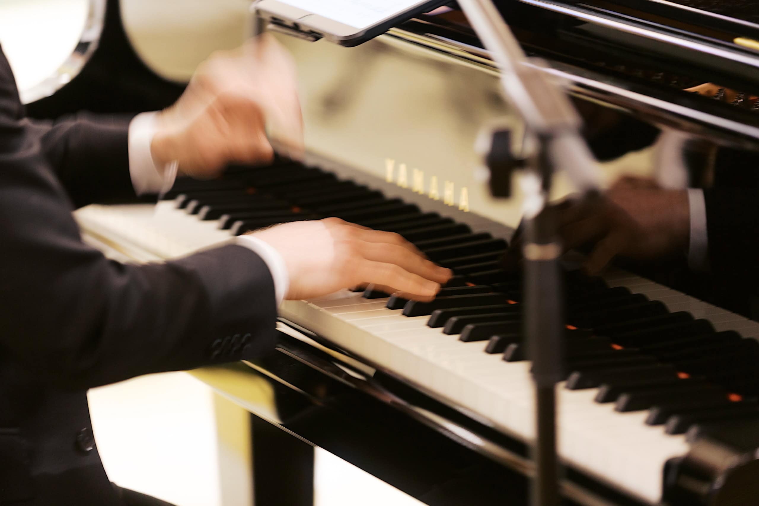 At The Ivy at Ellis Preserve spring wedding, a person in a suit plays a Yamaha grand piano, their hands moving gracefully over the keys with a microphone positioned nearby.