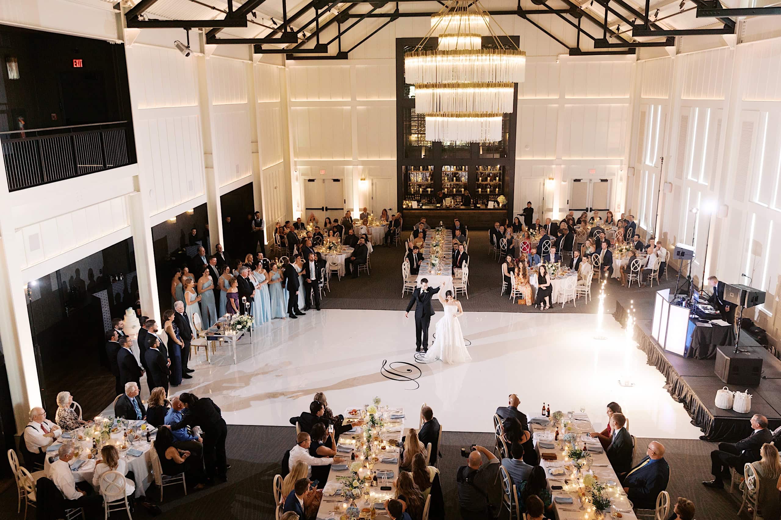 At The Ivy at Ellis Preserve spring wedding, a bride and groom share their first dance on a white floor in a large, elegant banquet hall surrounded by seated and standing guests.