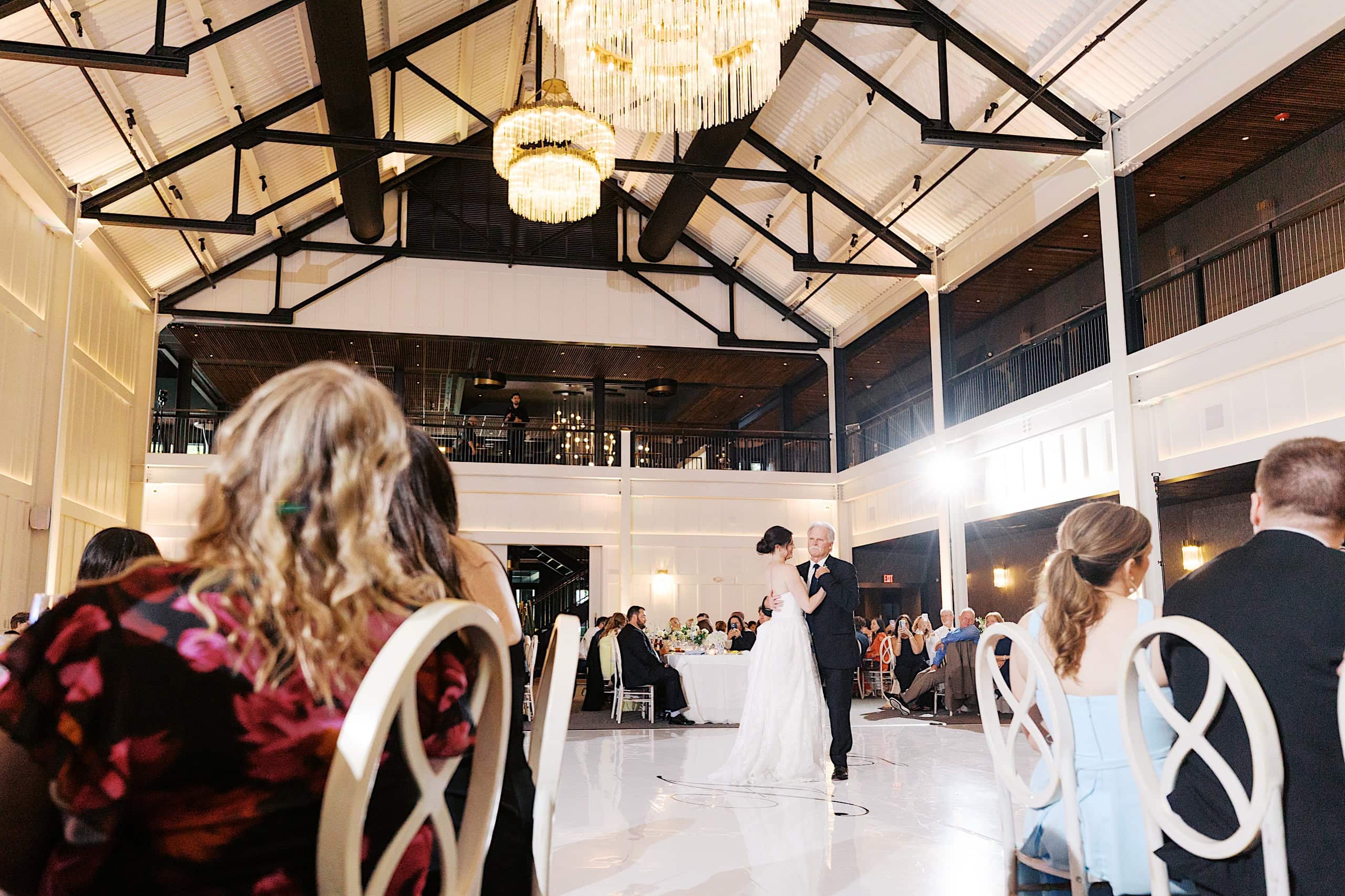A bride and groom share their first dance in a large, elegant reception hall at The Ivy at Ellis Preserve spring wedding, with guests seated at round tables watching.