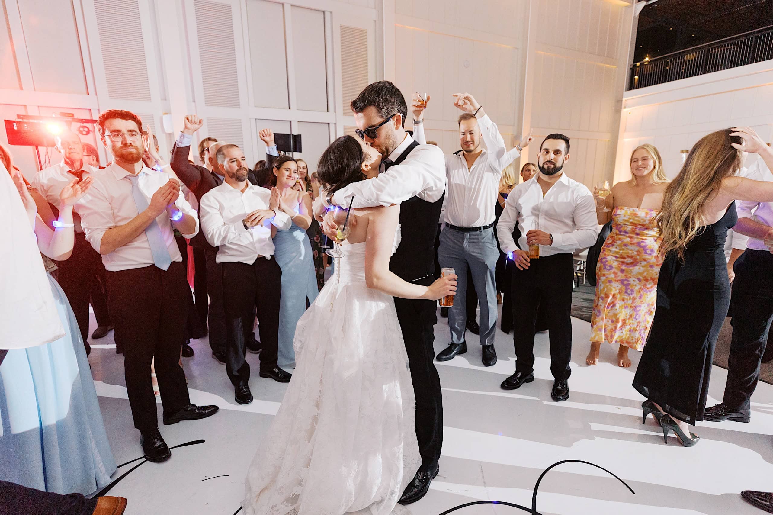 A bride and groom dance closely on a white floor at The Ivy at Ellis Preserve spring wedding, surrounded by cheering guests in a brightly lit reception hall.