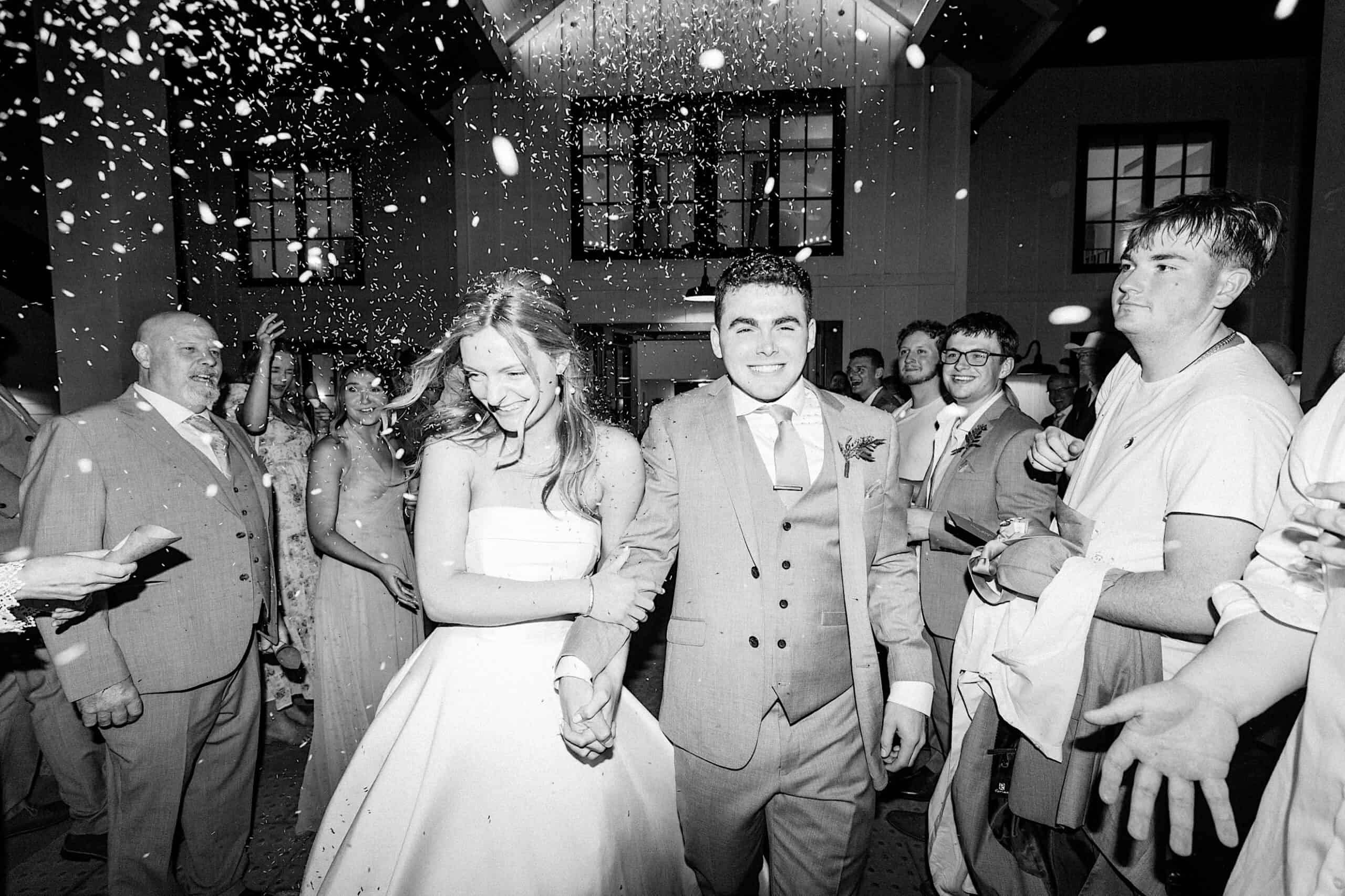 A bride and groom walk hand in hand through a crowd of guests throwing confetti during a magical Westwynd Gardens Spring Wedding evening celebration.