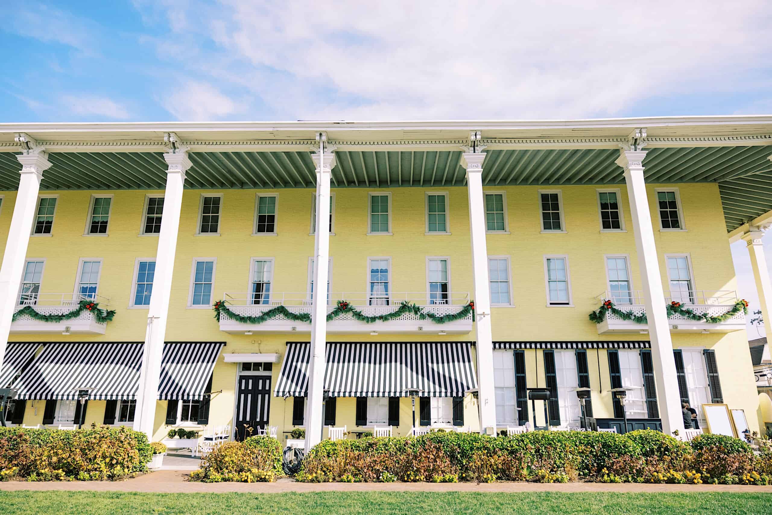 A large yellow building with tall white columns, black-and-white striped awnings, and garlands hanging from the balcony railings—perfect for a romantic November wedding at Congress Hall.