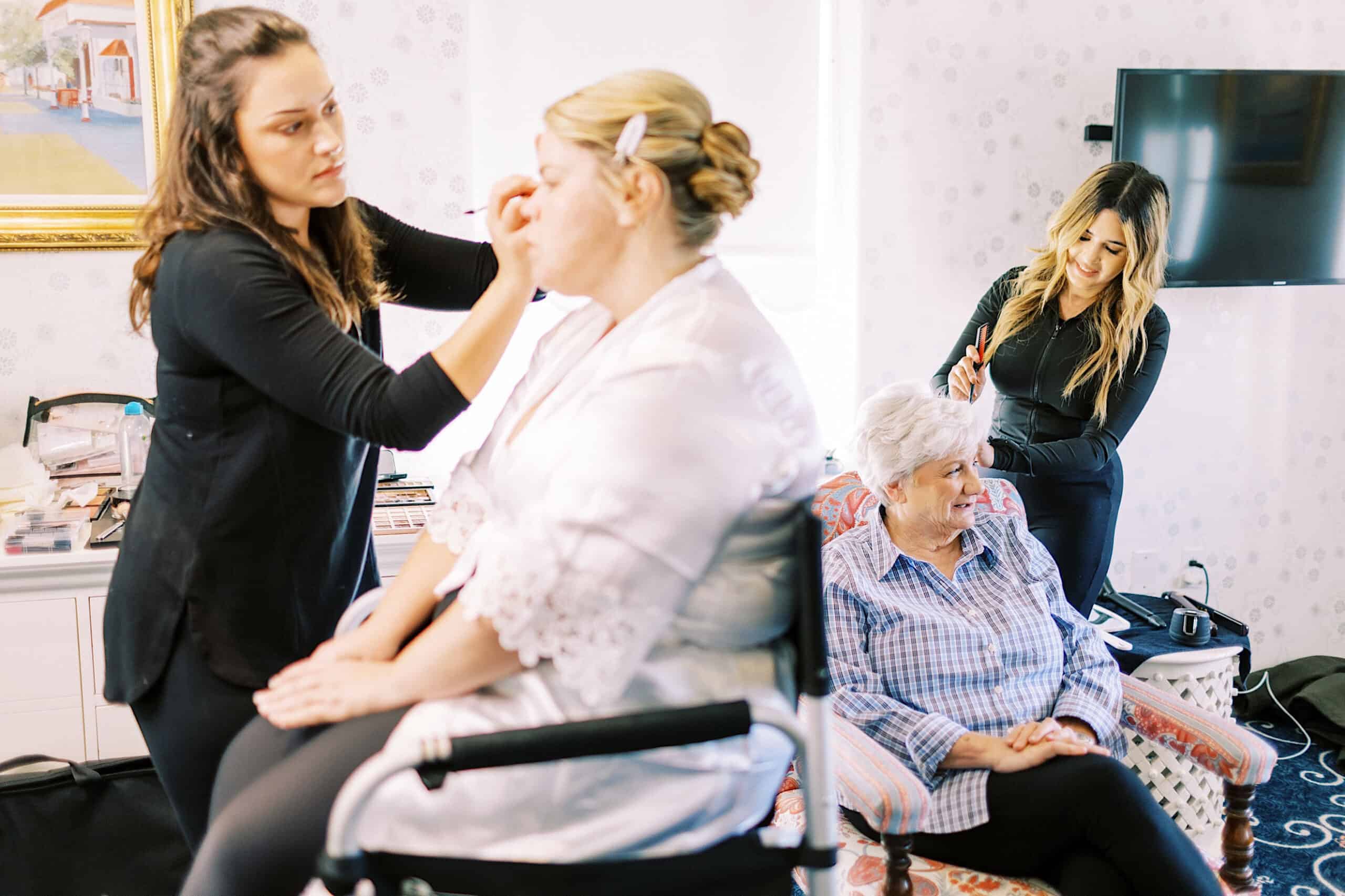Two women prepare another woman and an older woman for a romantic November wedding at Congress Hall, applying makeup and styling hair in a well-lit room.
