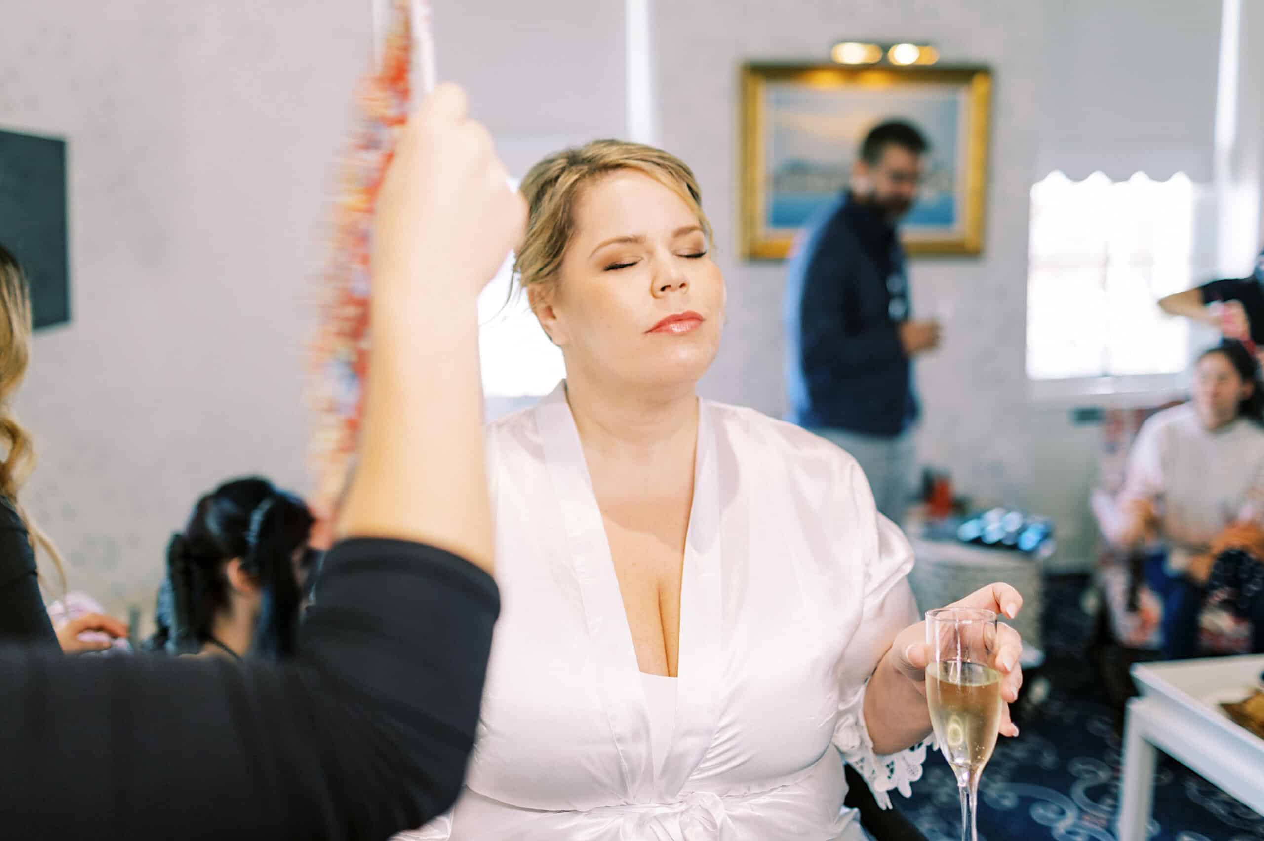 At a romantic November wedding at Congress Hall, a woman in a white robe holds a glass of champagne with her eyes closed while another person presents an object to her; several guests mingle in the background.