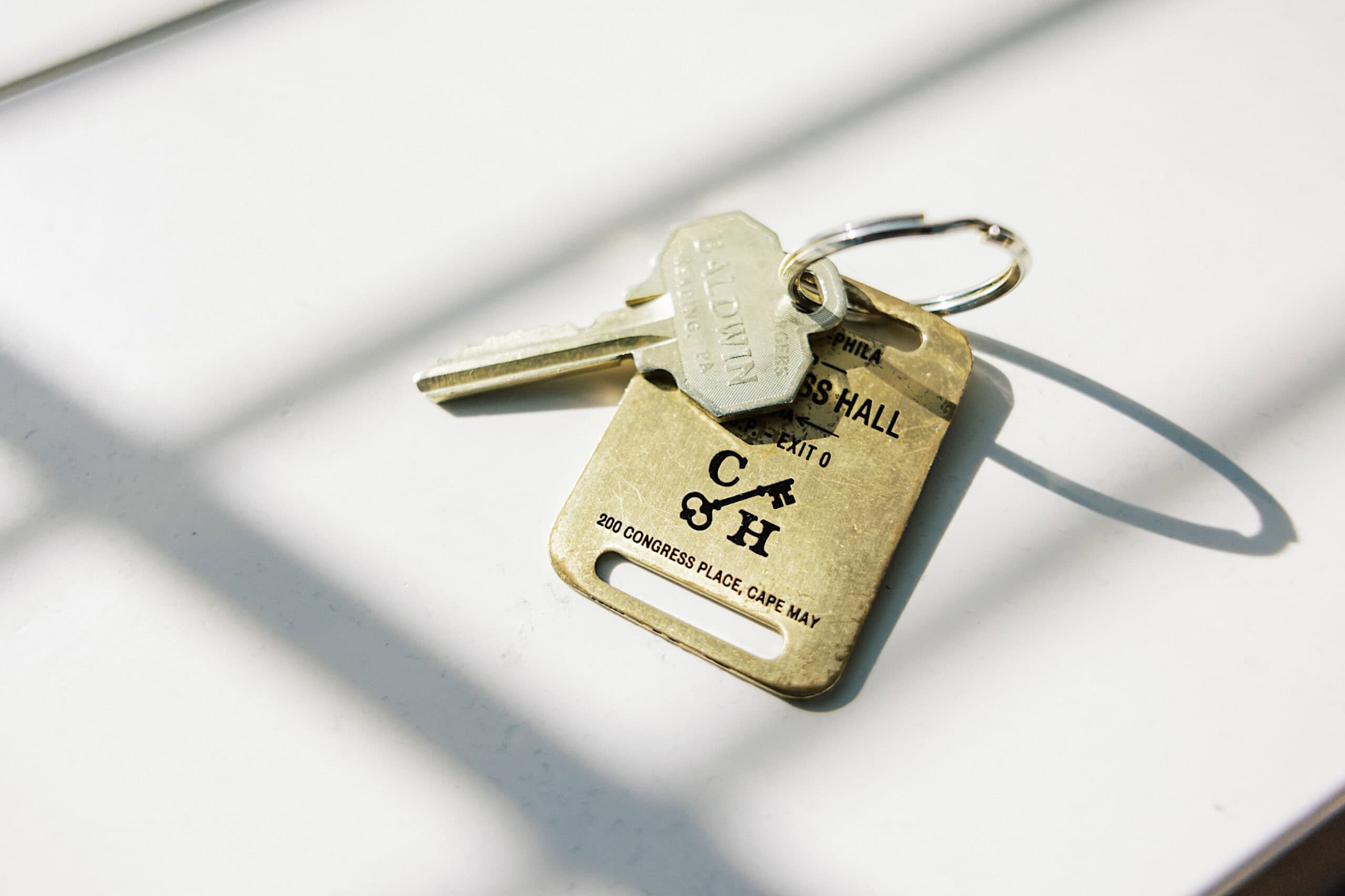 Two metal keys on a keyring attached to a brass hotel room tag labeled "C5 HALL" rest on a white surface, evoking memories of a romantic November wedding at Congress Hall.