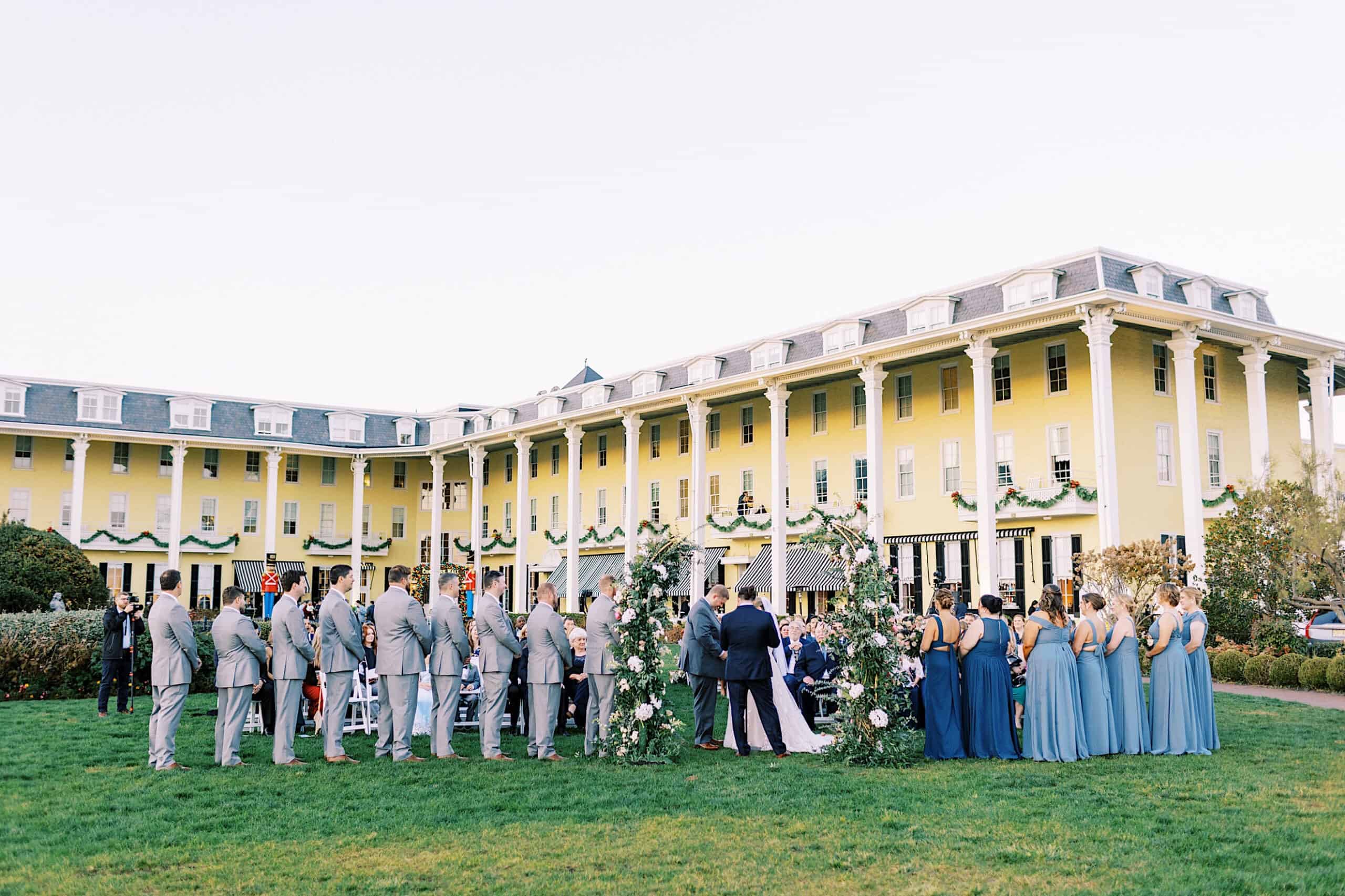 A romantic November wedding at Congress Hall unfolds on the lawn, with guests and the wedding party gathered before a grand yellow historic building.