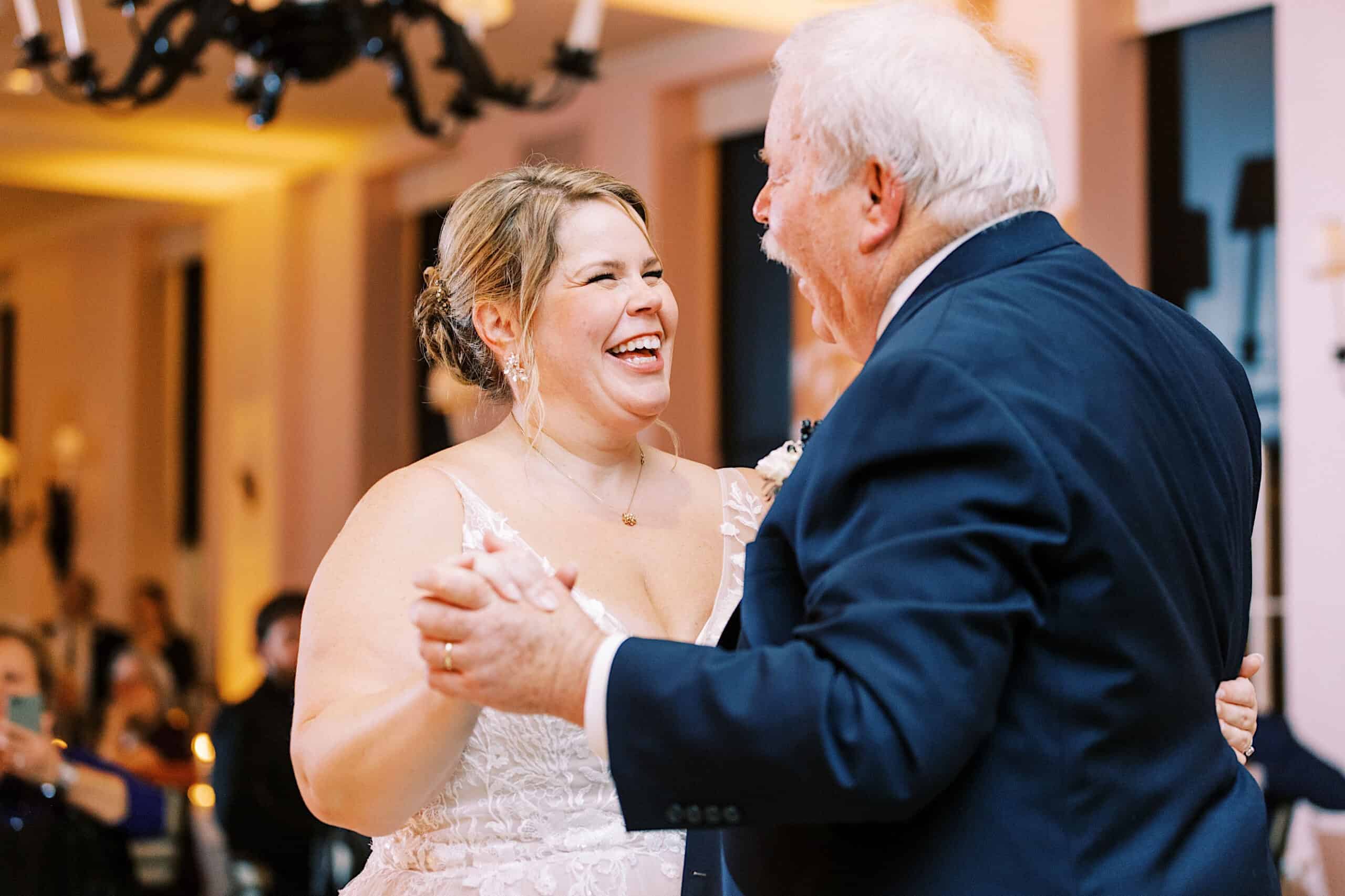 A bride in a white dress and an older man in a suit smile and dance together at their romantic November wedding at Congress Hall.